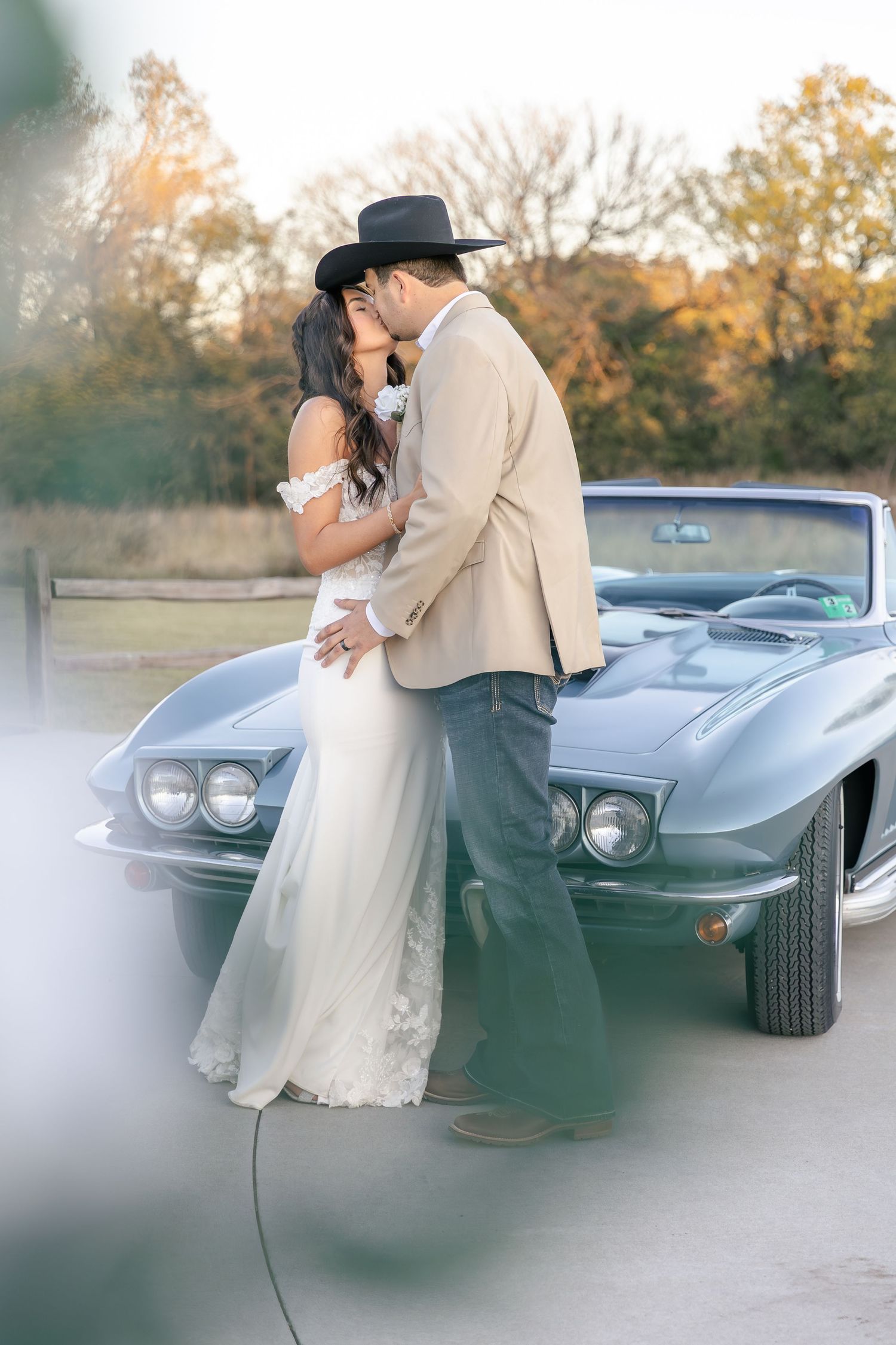Classic car wedding photo with couple embracing beside vintage Corvette.