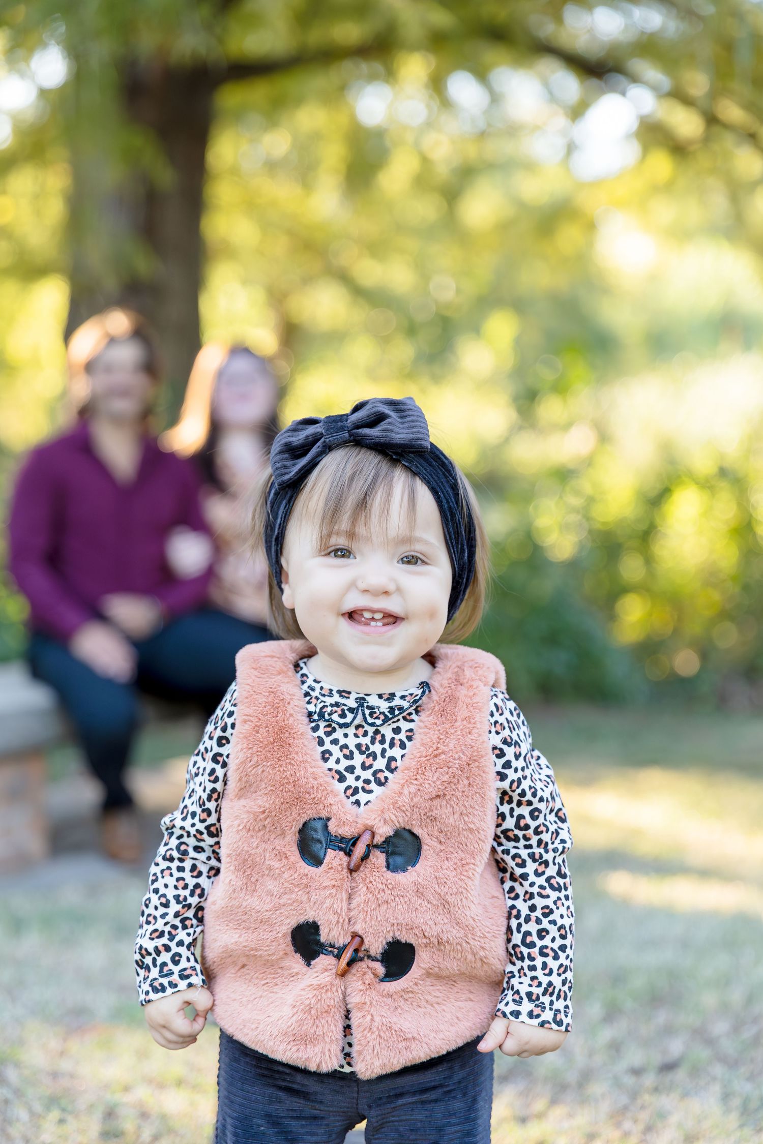 Child wearing leopard print and pink vest smiling during outdoor photoshoot.