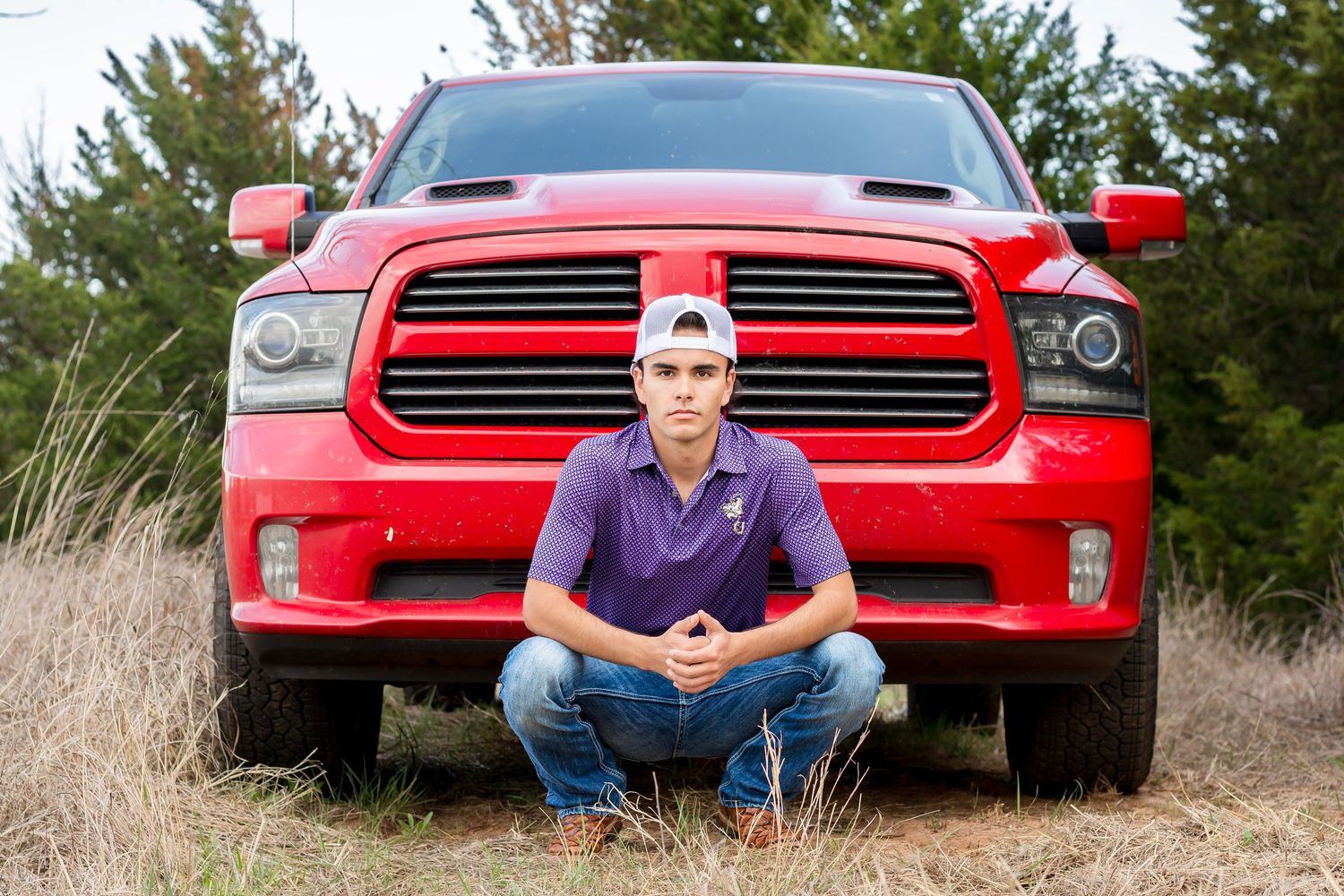 Outdoor senior portrait session with red pickup truck and purple polo shirt.