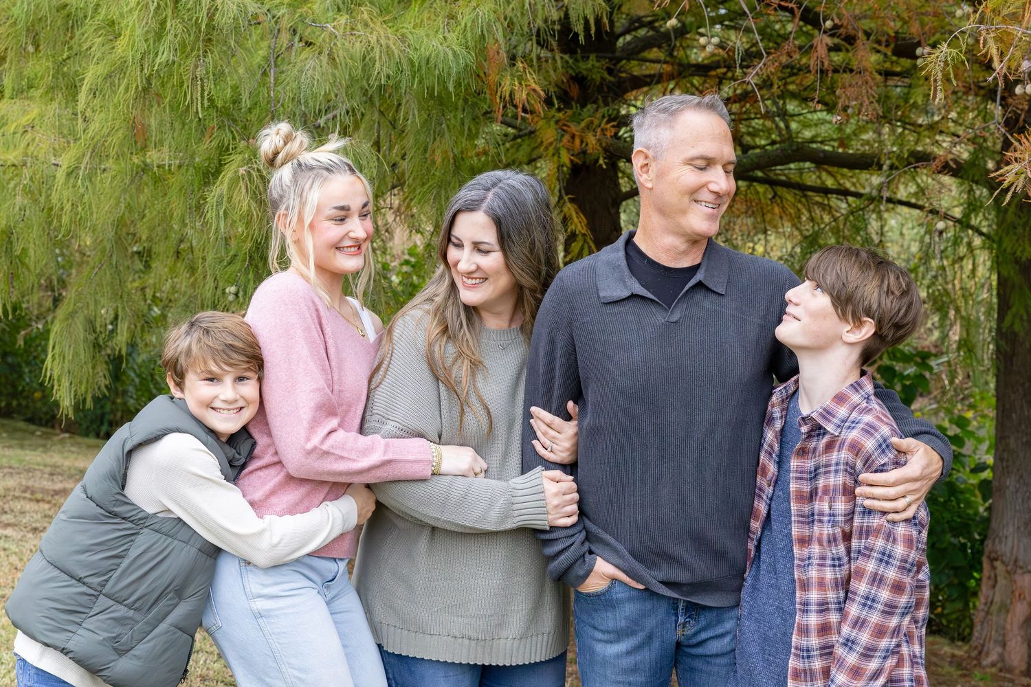 Family group hugging and laughing together during outdoor photo session.