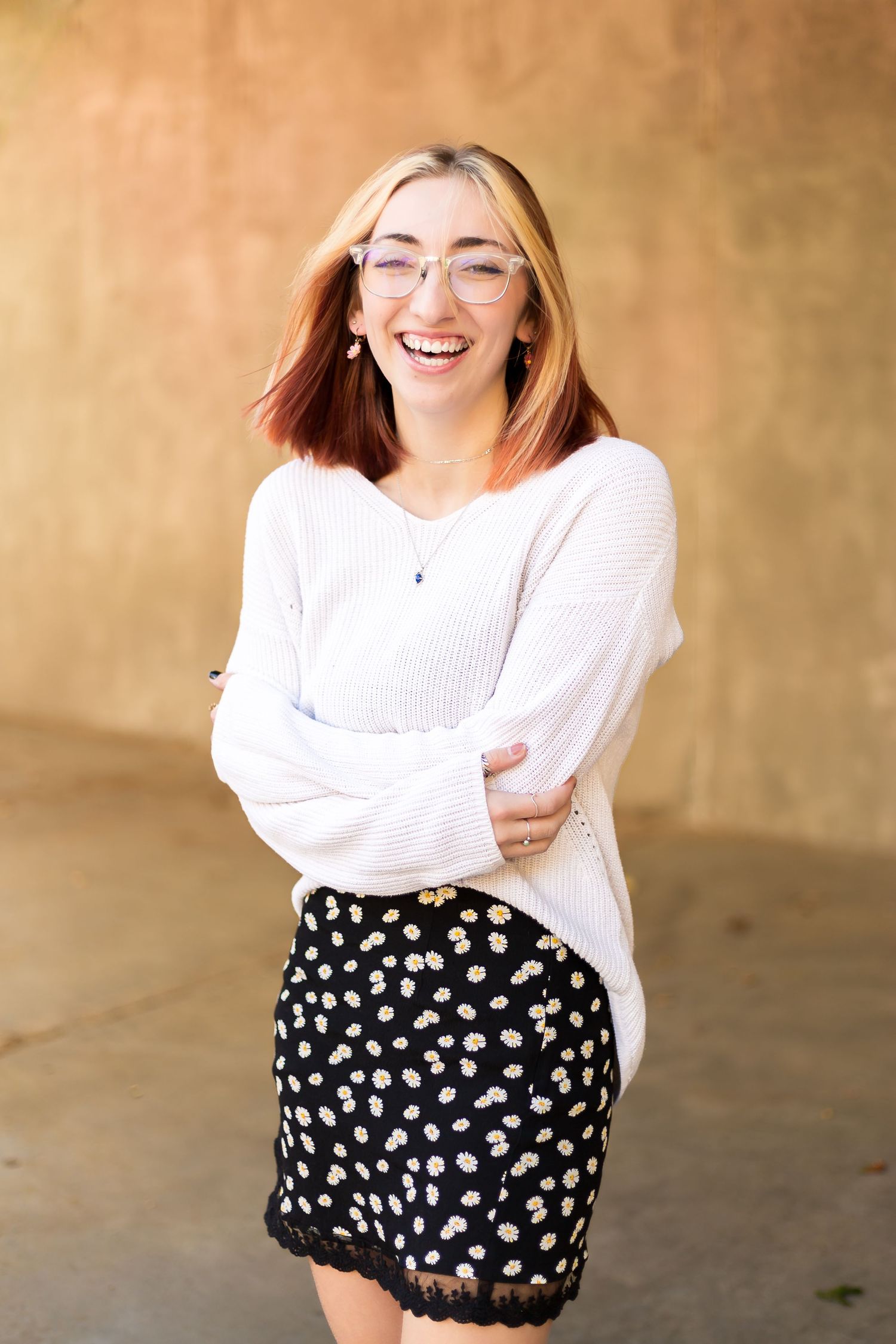 a senior in white sweater and polka dot skirt laughing and posing in a casual photoshoot sequence.