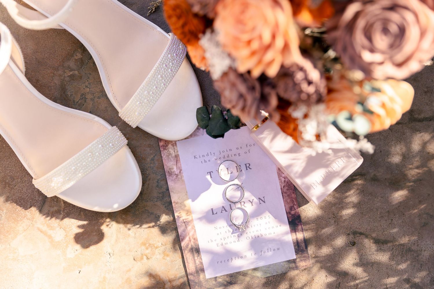 Wedding details including flowers and invitations arranged on textured surface with natural lighting.