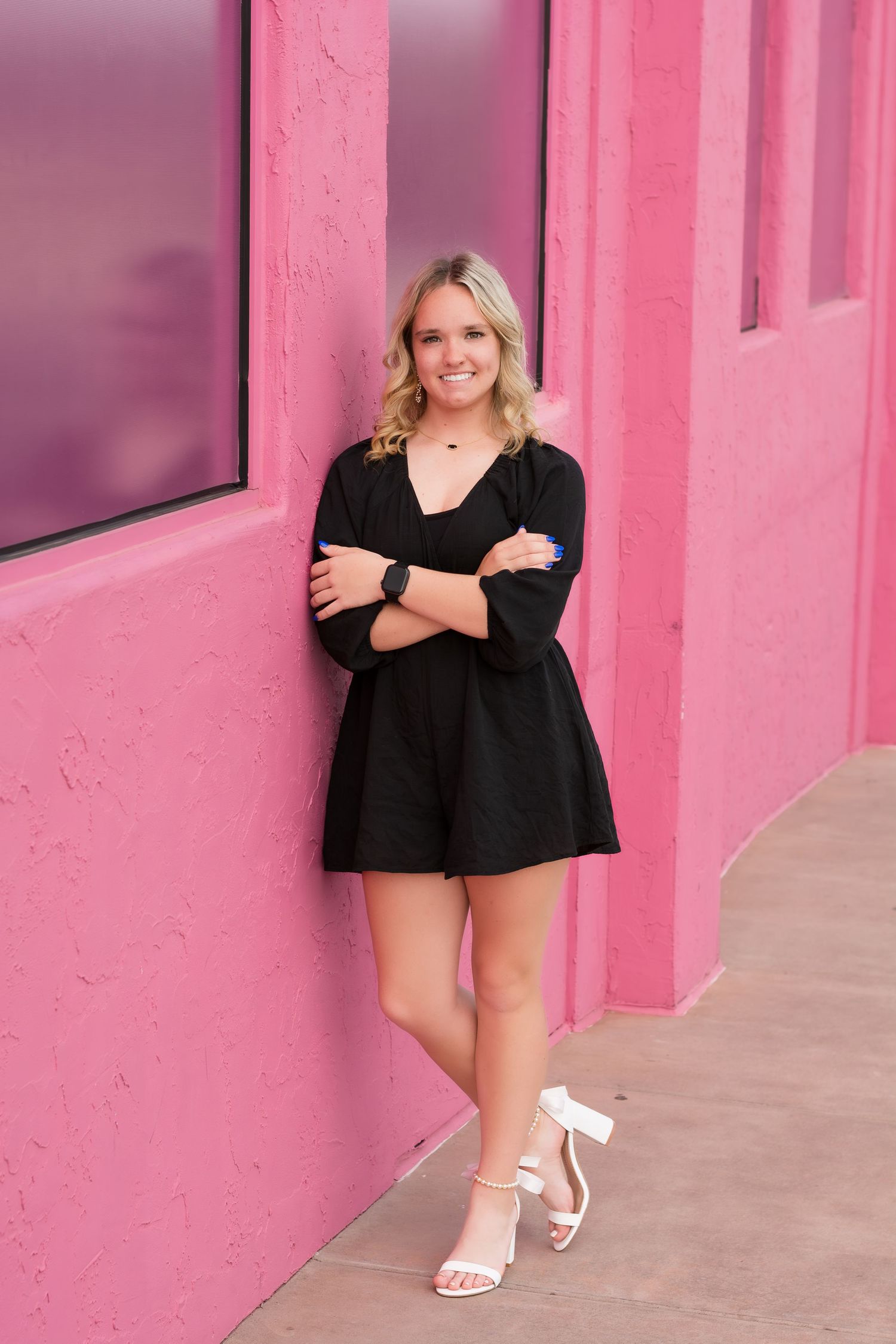 Senior Portrait series against a pink wall wearing a black outfit and white sandals.