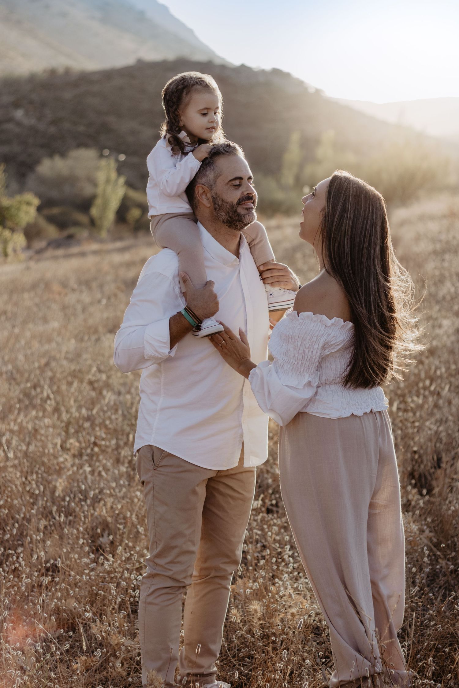 Familia con una niña sobre los hombros del padre durante una sesión familiar al atardecer en la naturaleza.