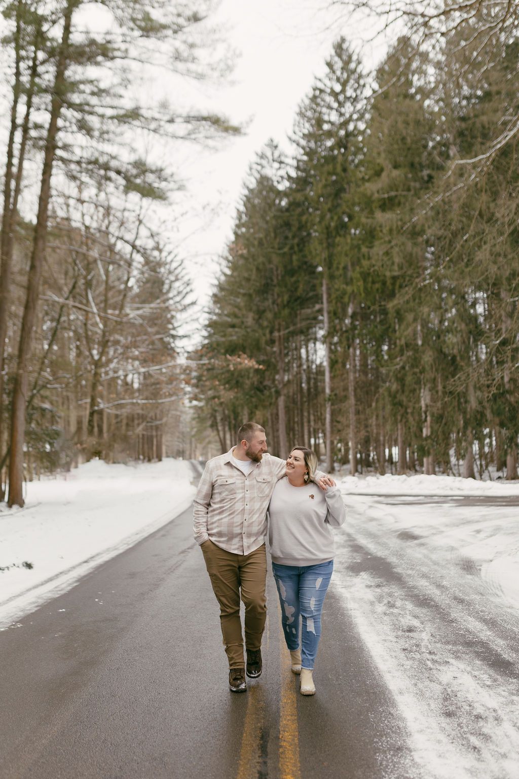 A couple walks together on a snowy winter road through a forest.