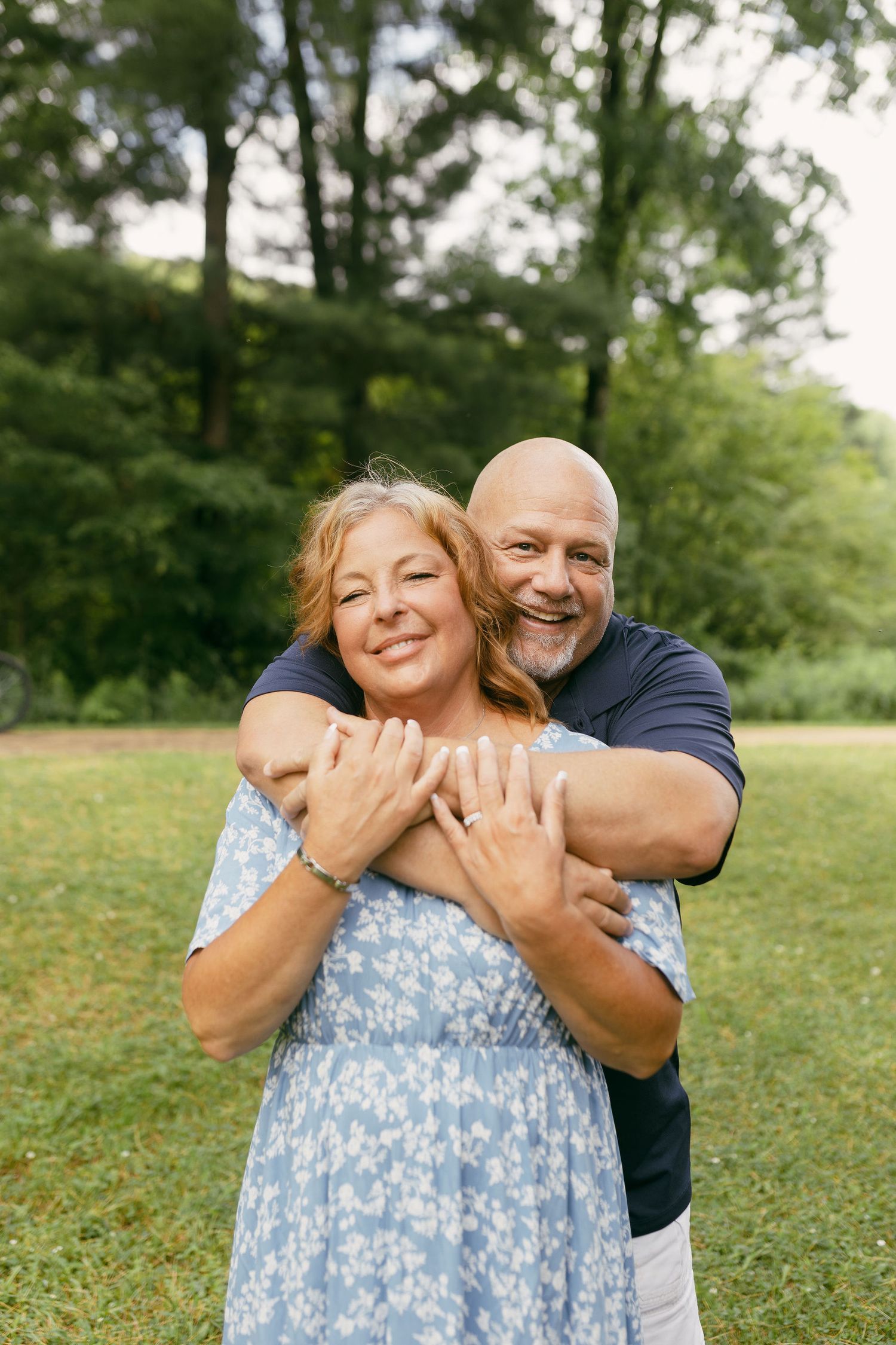 Couple embracing playfully on a grassy lawn in summer, with woman wearing a blue floral dress.