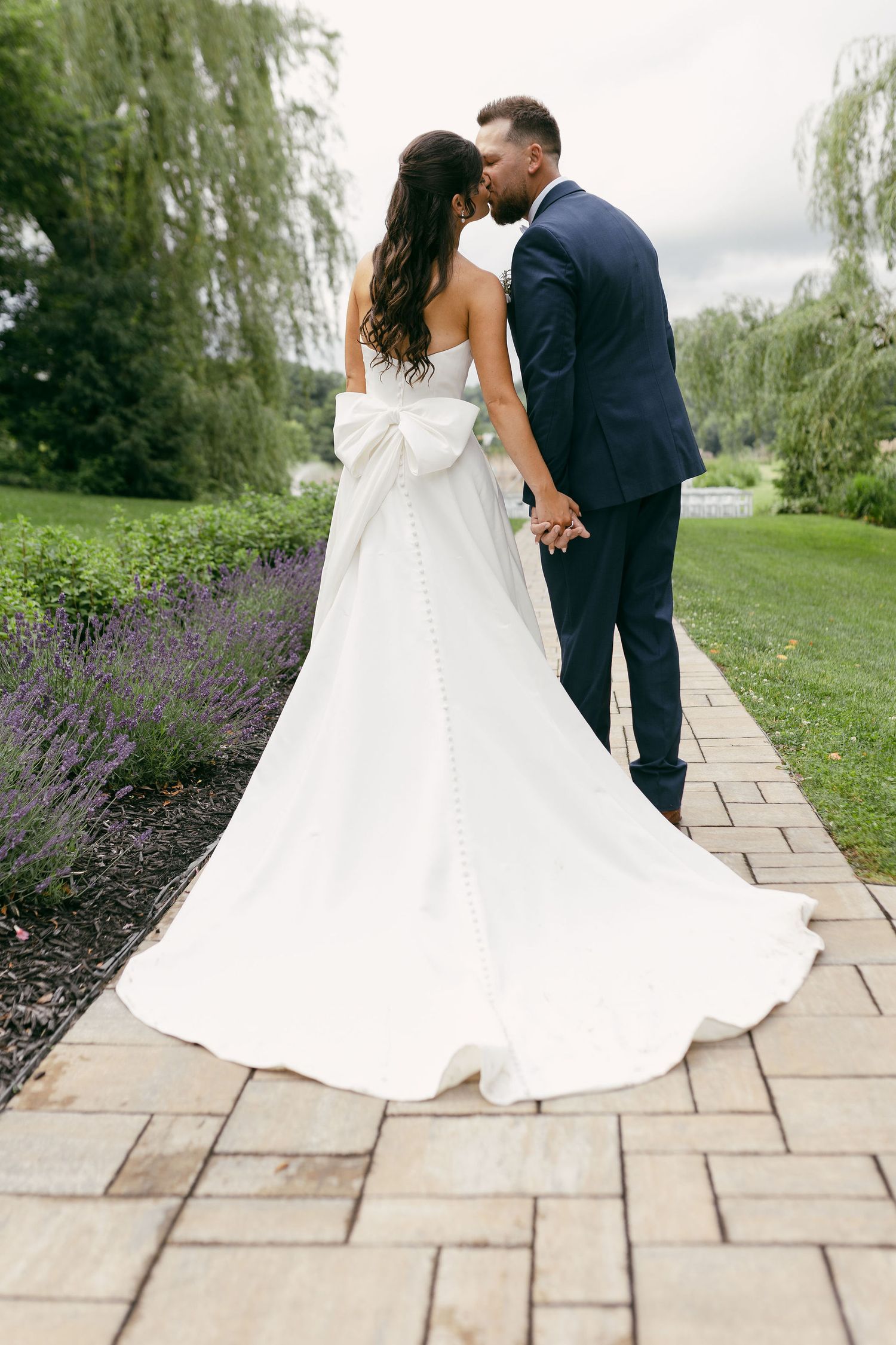 White wedding dress twirls gracefully on stone pathway surrounded by garden landscaping.