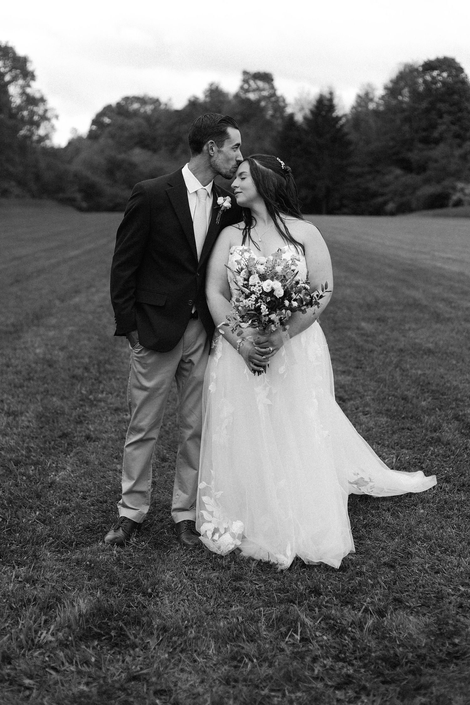 Black and white photo of newlyweds walking together on a grassy hillside.