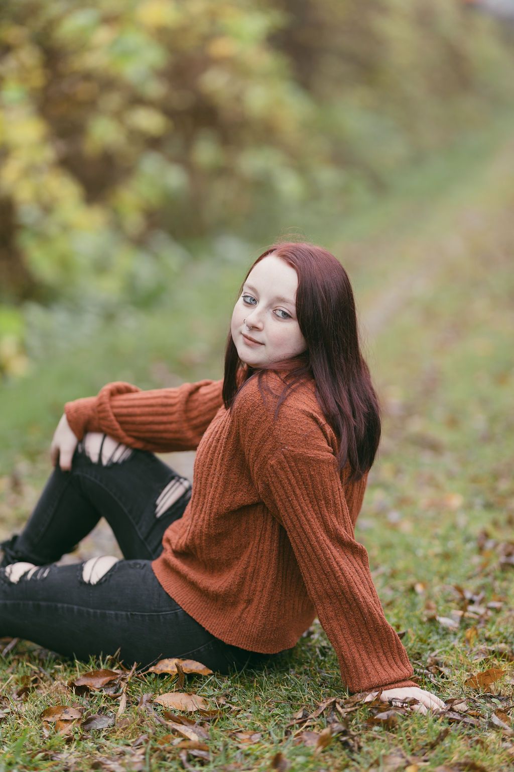 Autumn lifestyle photos with rust sweater and black pants on grass with fallen leaves.