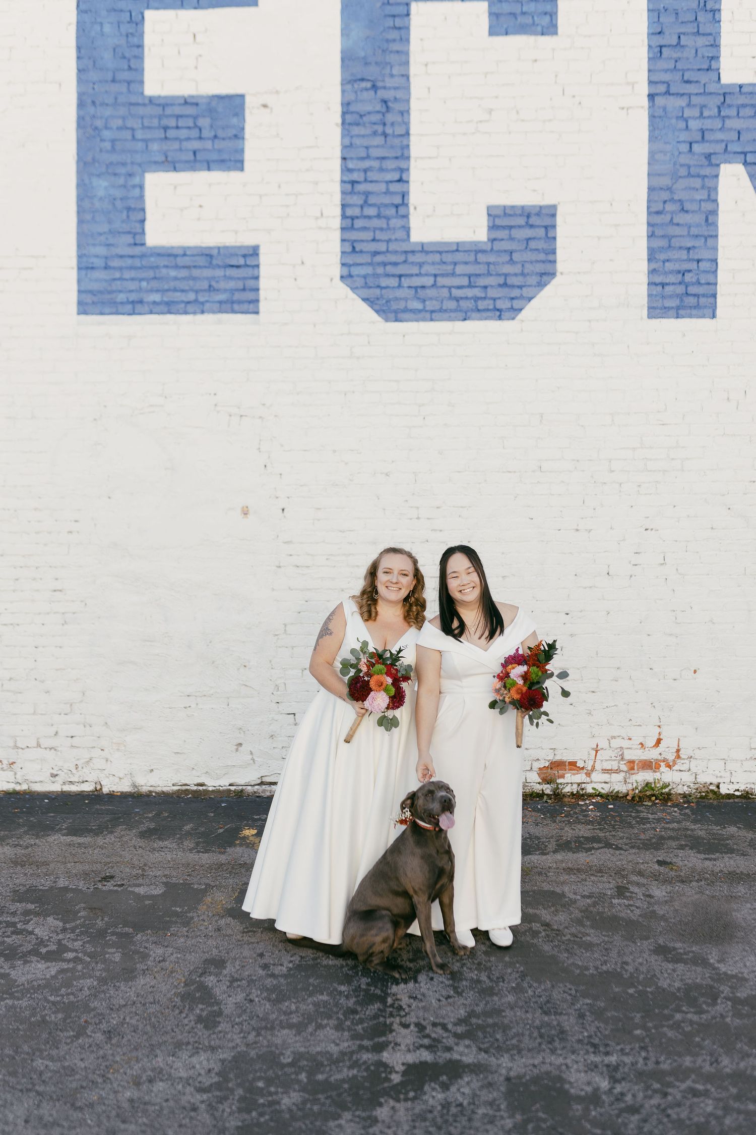 A wedding photo series against a white brick wall featuring a couple in white dresses with their brown dog.