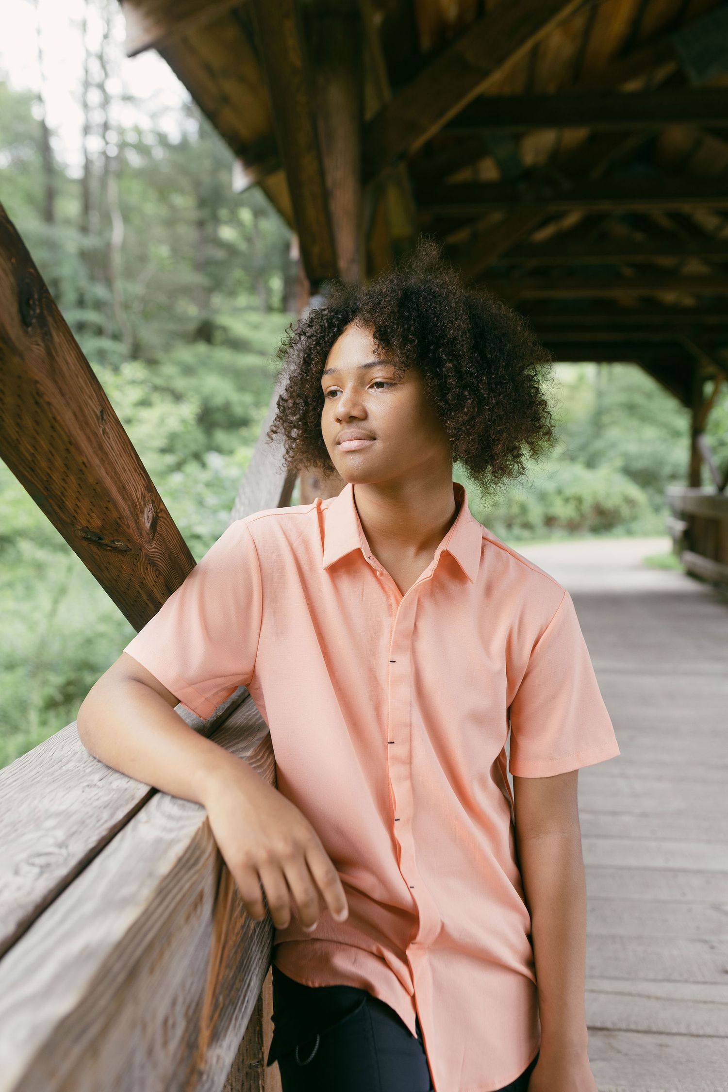 Person in peach colored shirt leaning against wooden covered bridge railing.