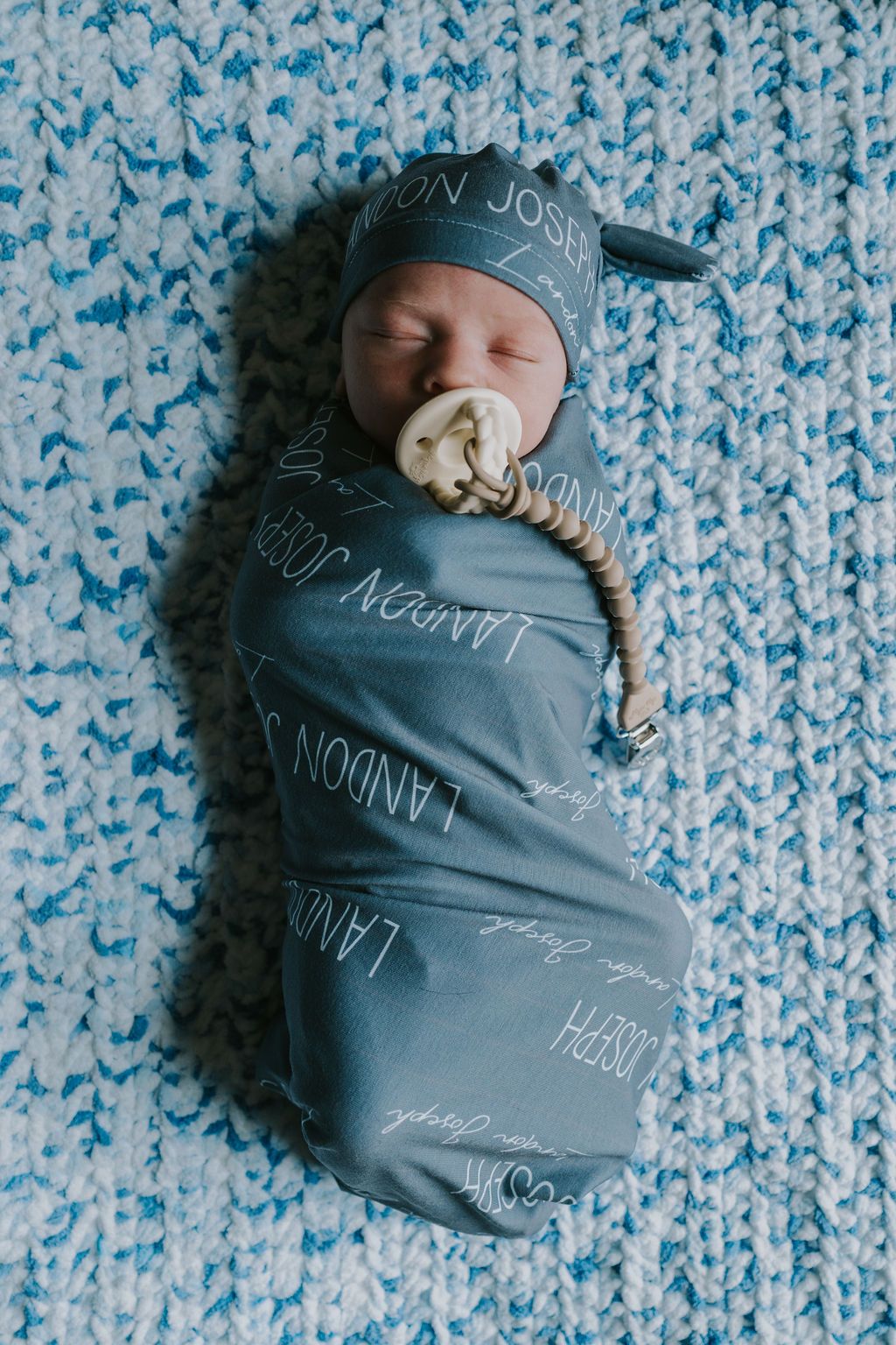 Sleeping newborn wrapped in gray swaddle blanket on blue knit background.
