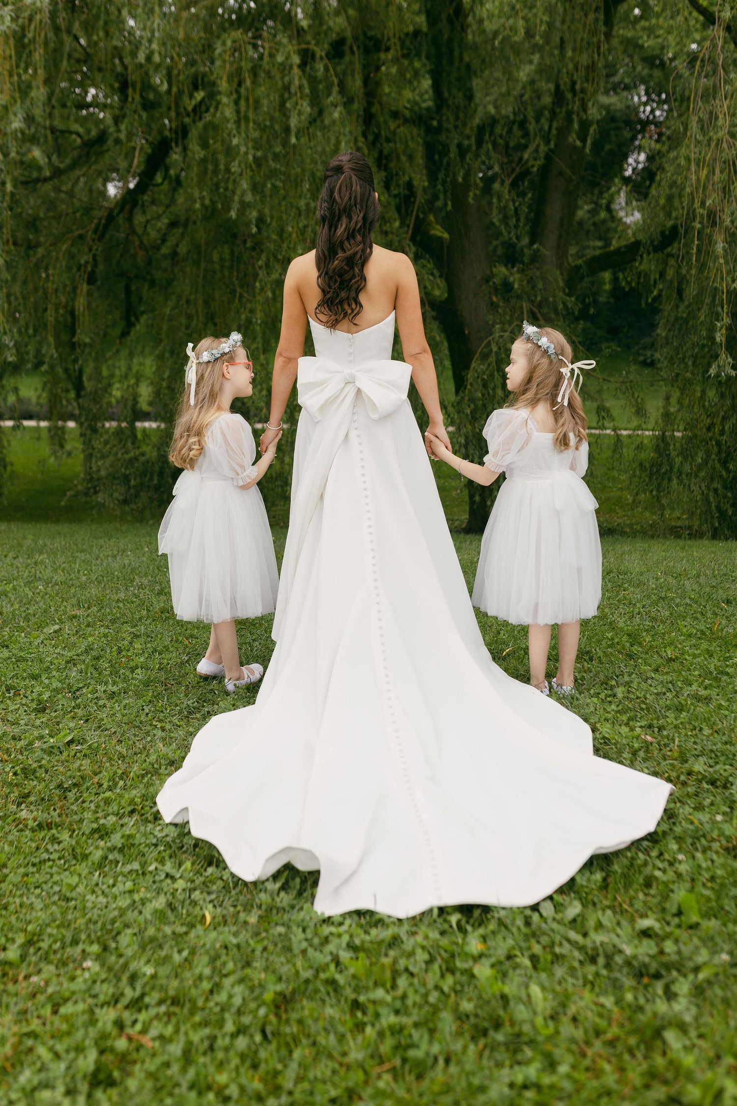 Three white wedding dresses photographed from behind against lush green grass.