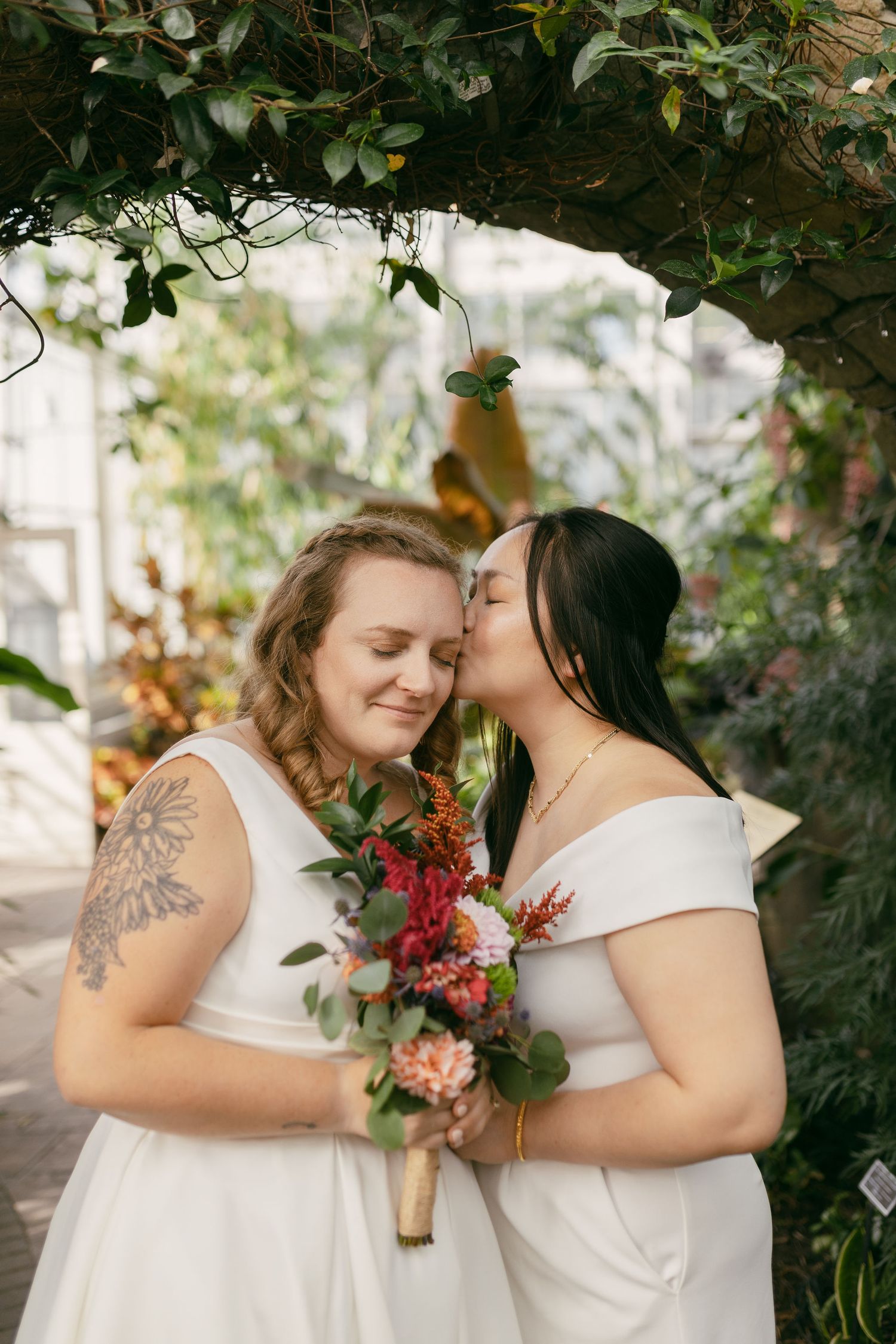 Intimate garden wedding portrait with red floral bouquets and natural greenery.
