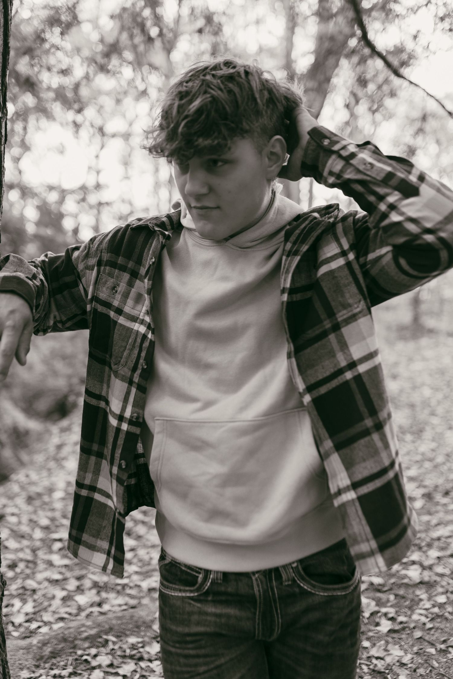 Teen boy in plaid shirt and white hoodie poses in autumn forest, black and white photo.