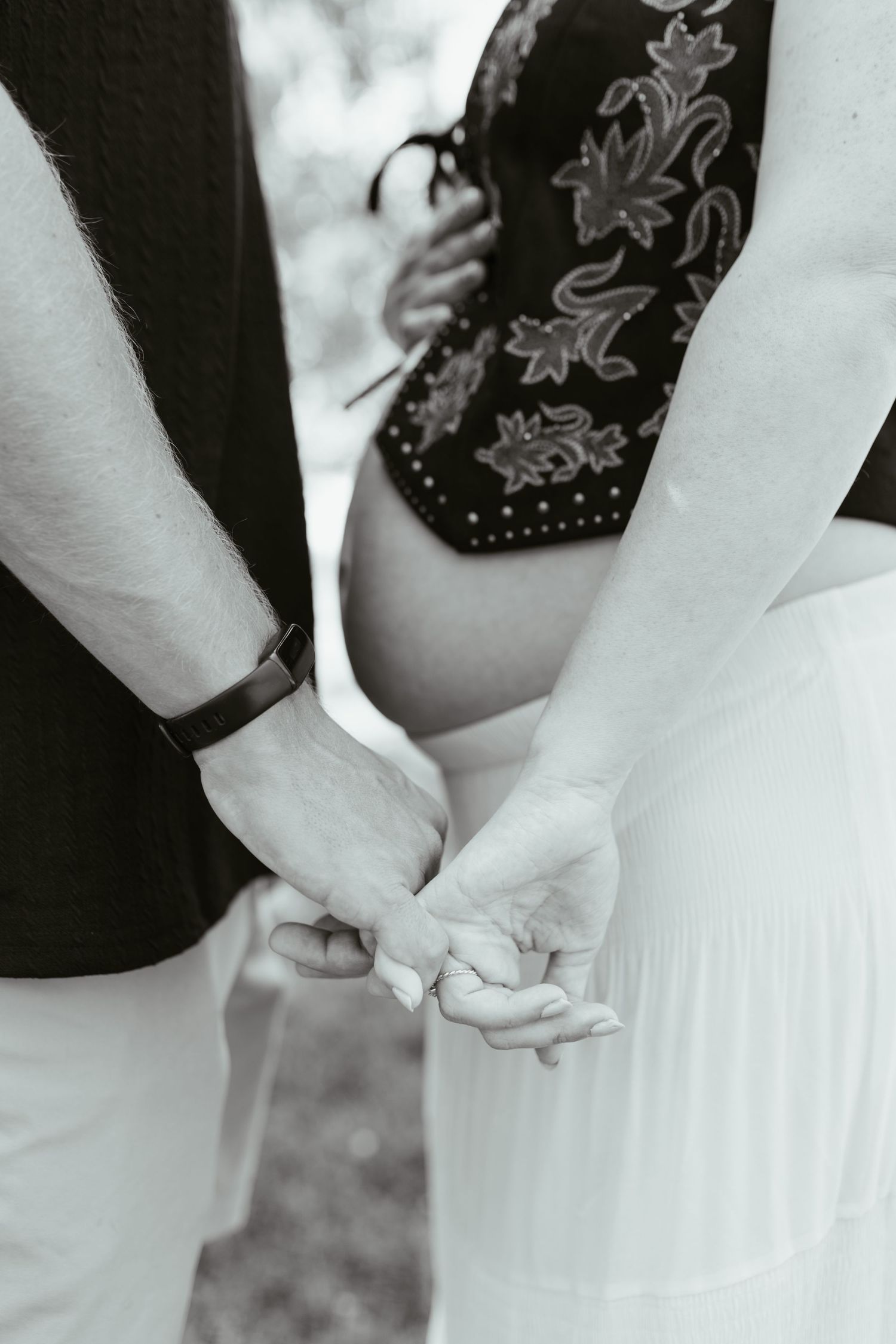 Black and white photo of a couple holding hands, showing a pregnant belly, capturing a tender maternity moment.