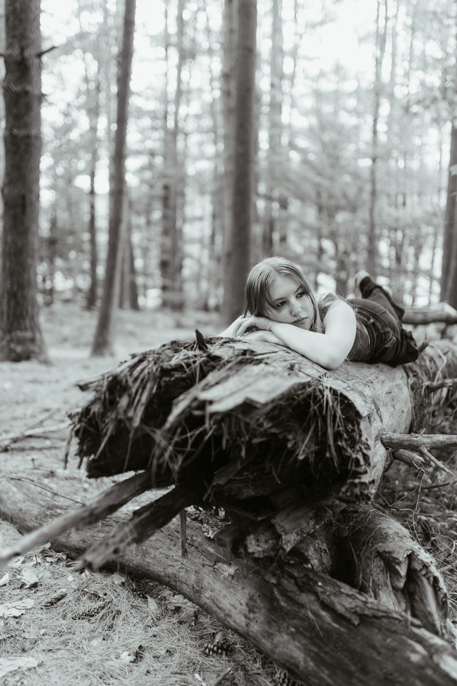 Black and white photo of a young girl resting on a fallen tree in a forest.