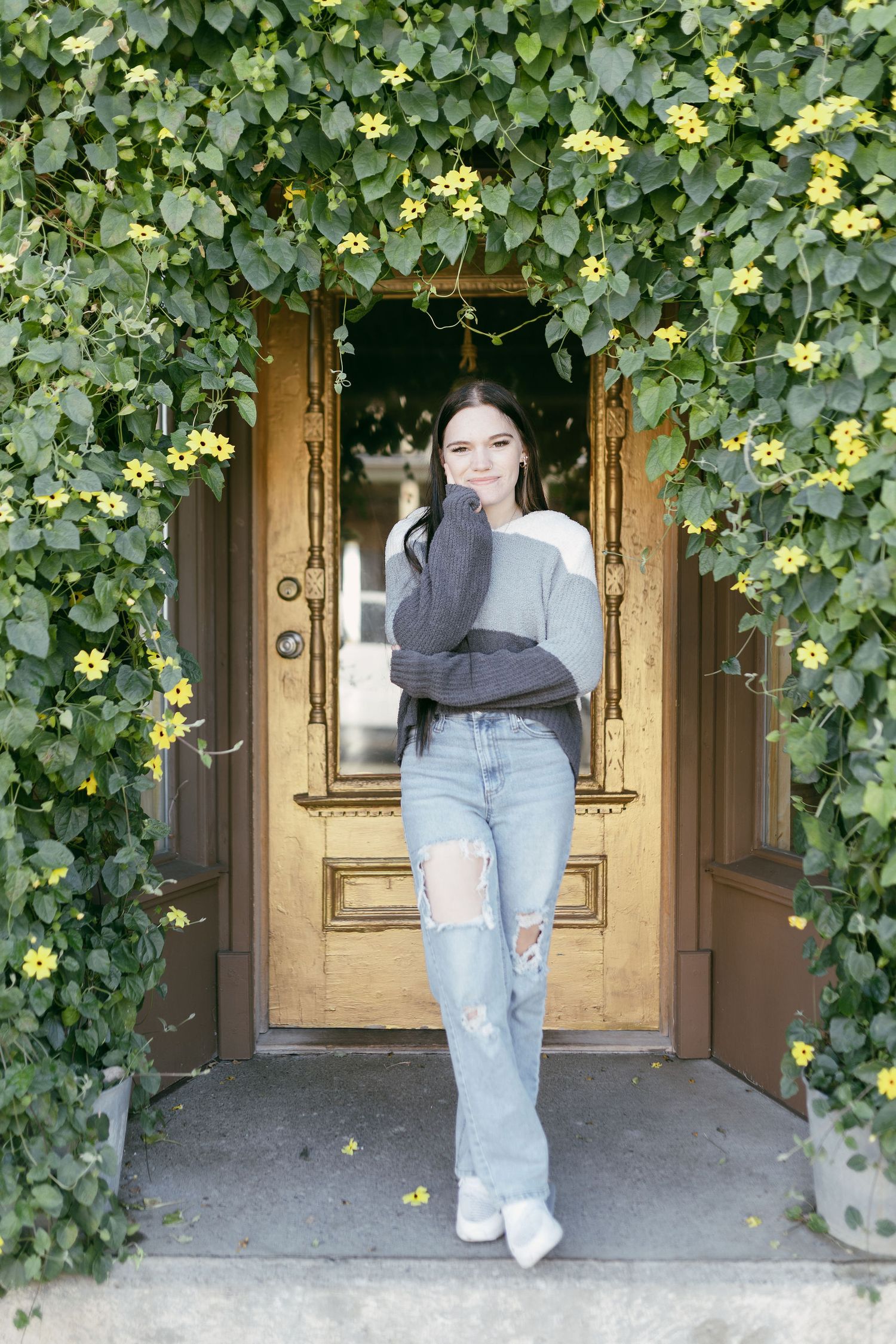 A series of poses showing a casual autumn outfit with a gray sweater and jeans against a vine-covered doorway.
