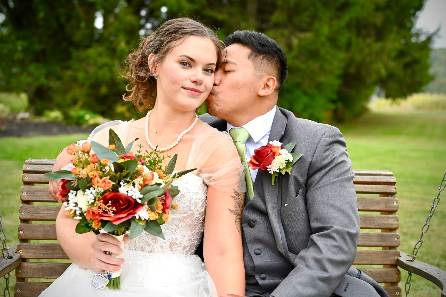 Wedding couple shares intimate moments on a park bench surrounded by greenery.