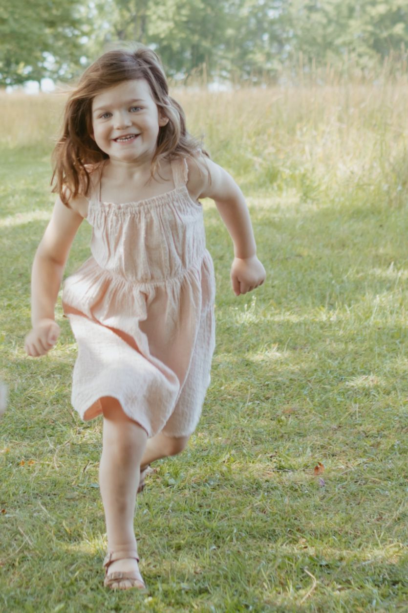 A happy young girl in a pink dress runs joyfully through a sunny green park.