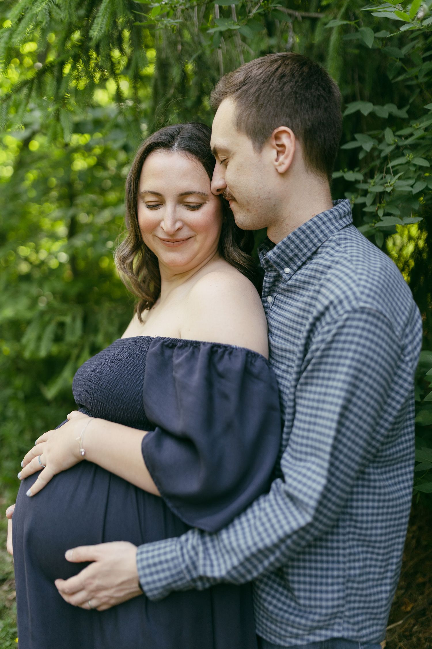 Intimate outdoor portrait of a couple embracing among green trees and natural scenery.