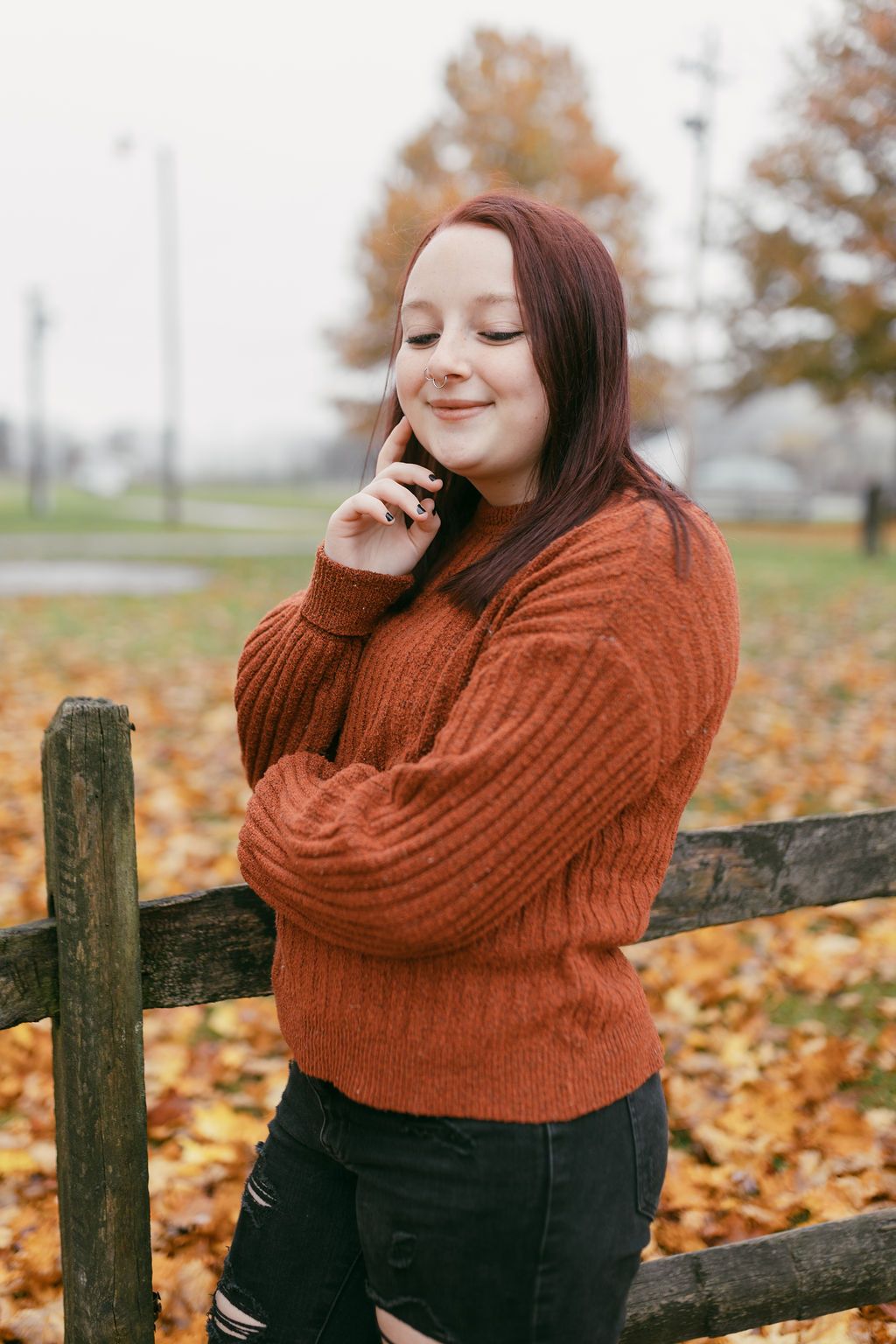 Autumn fashion shoot featuring a rust sweater and distressed jeans against a rustic fence.