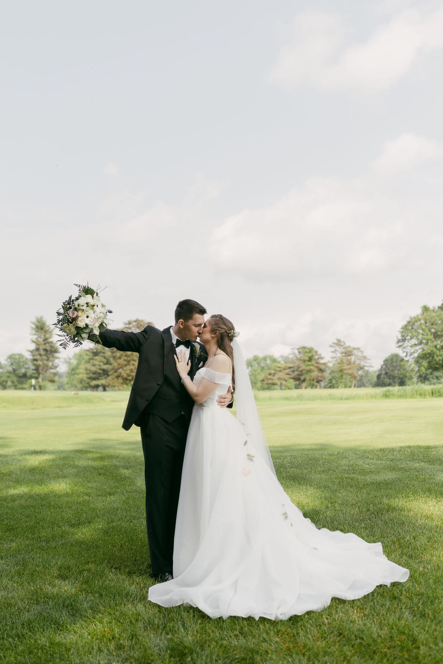 Newlyweds share an intimate moment while posing for portraits on a sunlit golf course.