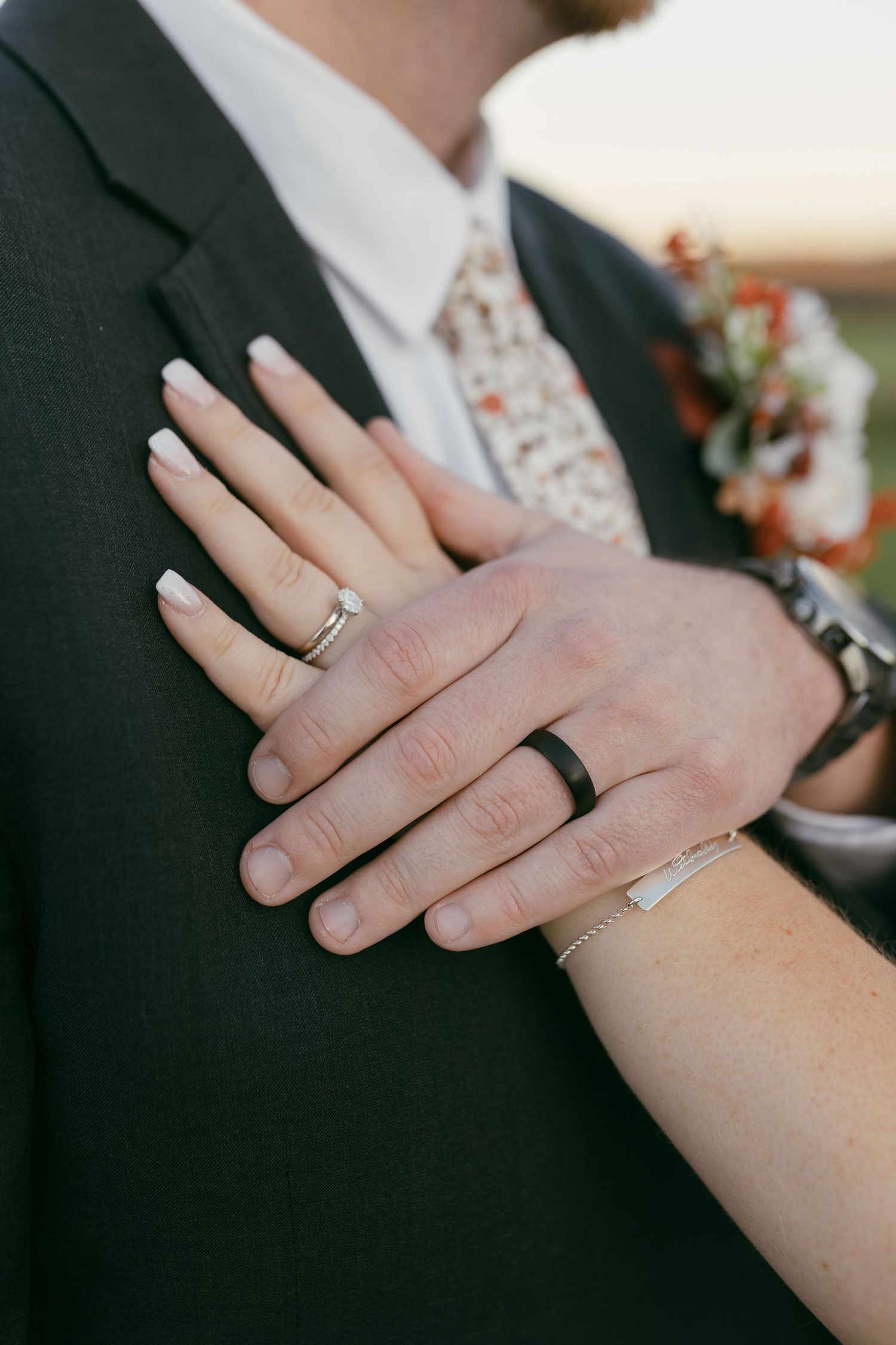 Close-up of wedding rings and hands showing both gold and black bands against formal attire.