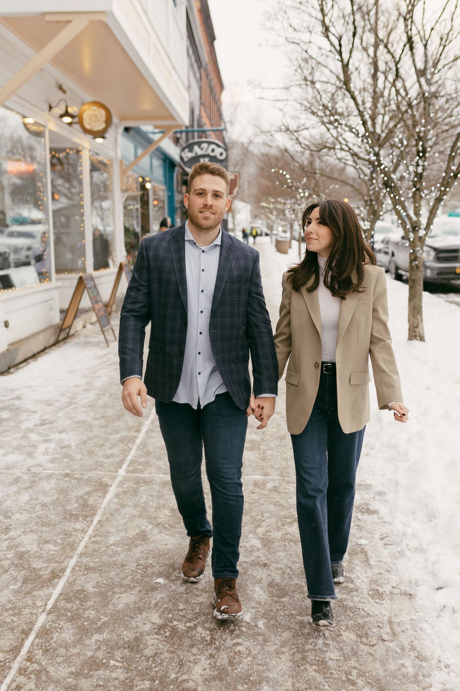 Couple walking together on a snowy winter sidewalk in formal attire.