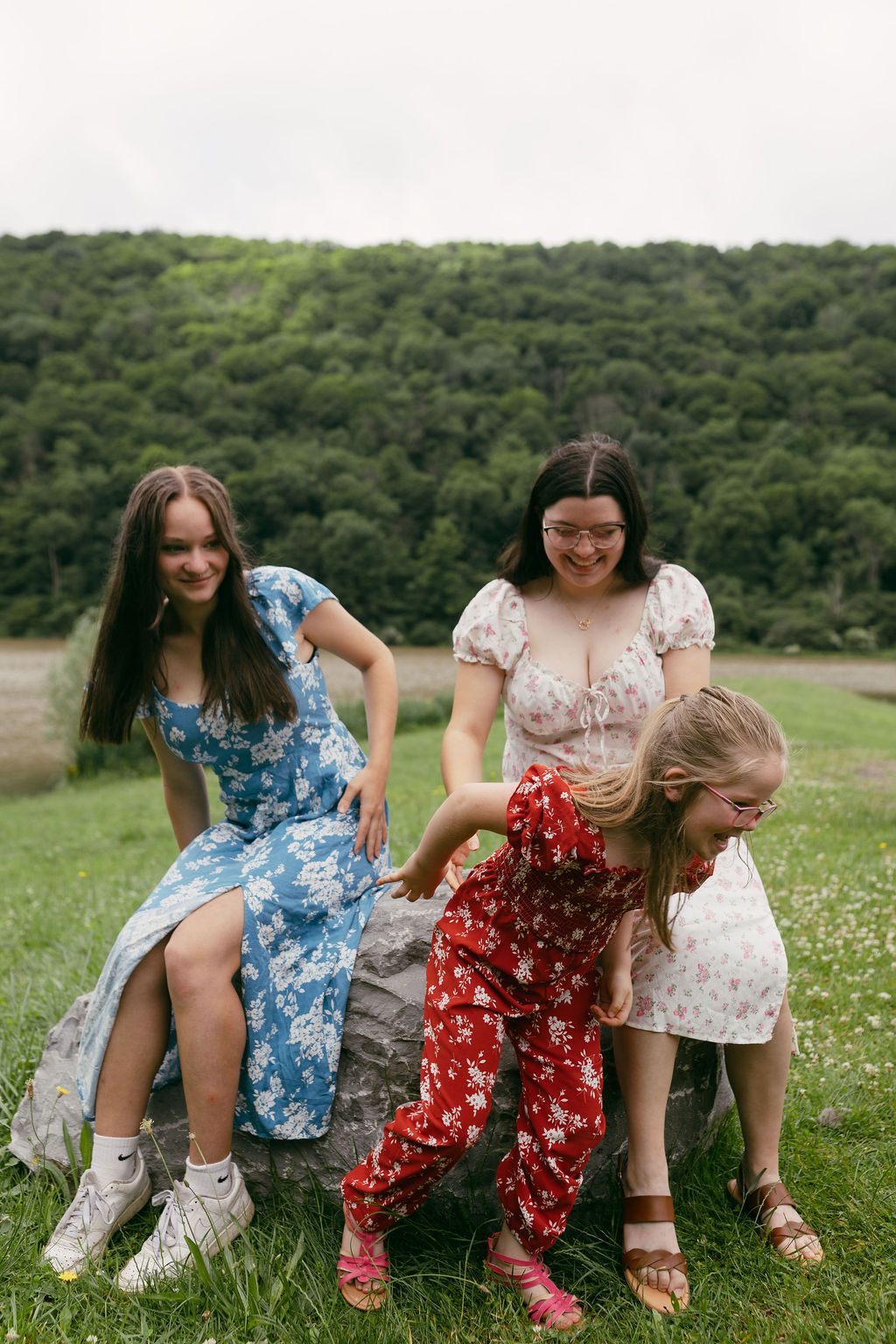 People in floral dresses bend down to pick flowers in a sunny meadow.