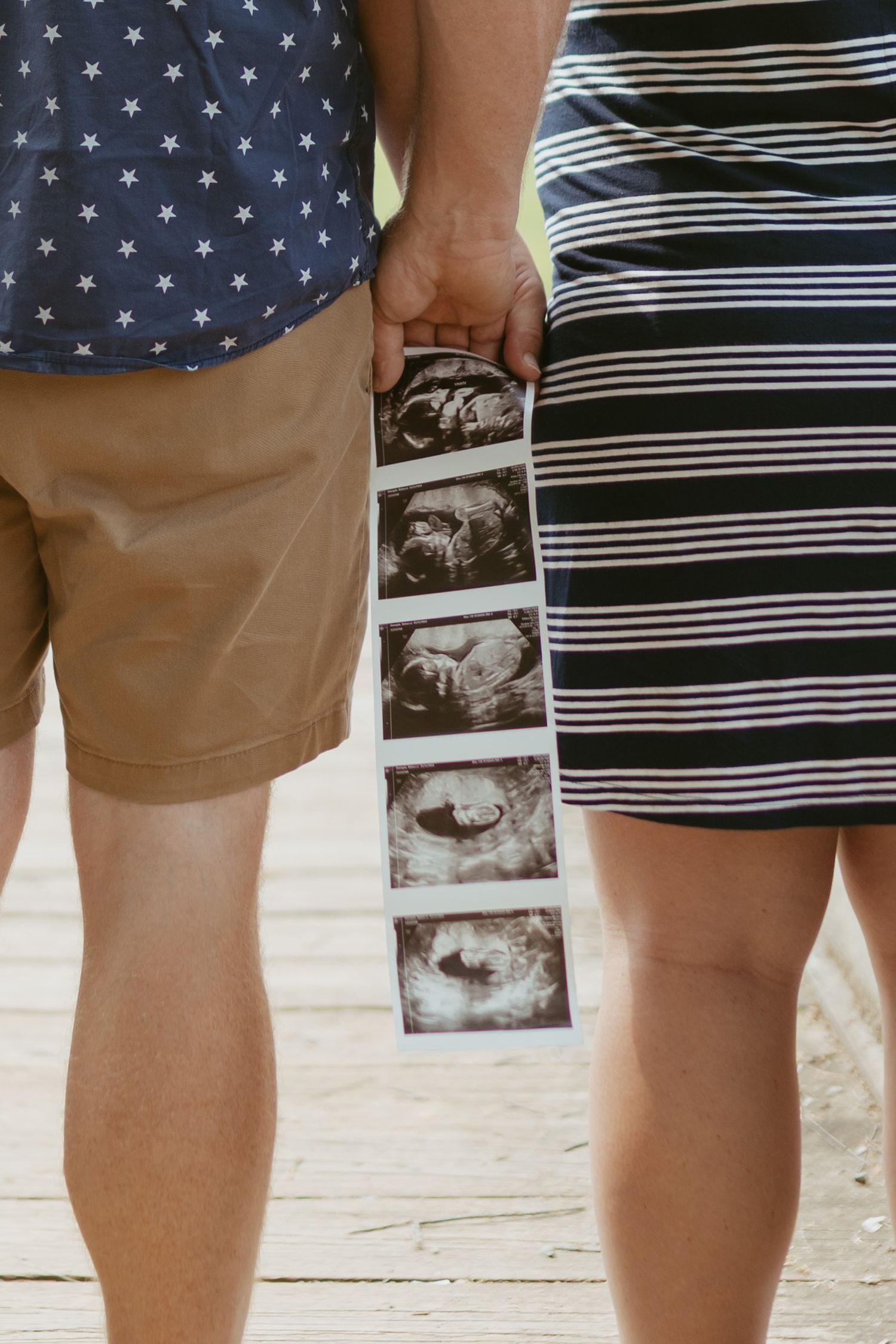 Couple holding ultrasound photos together, pregnancy announcement with sonogram strip, man in star shirt and woman in striped dress.