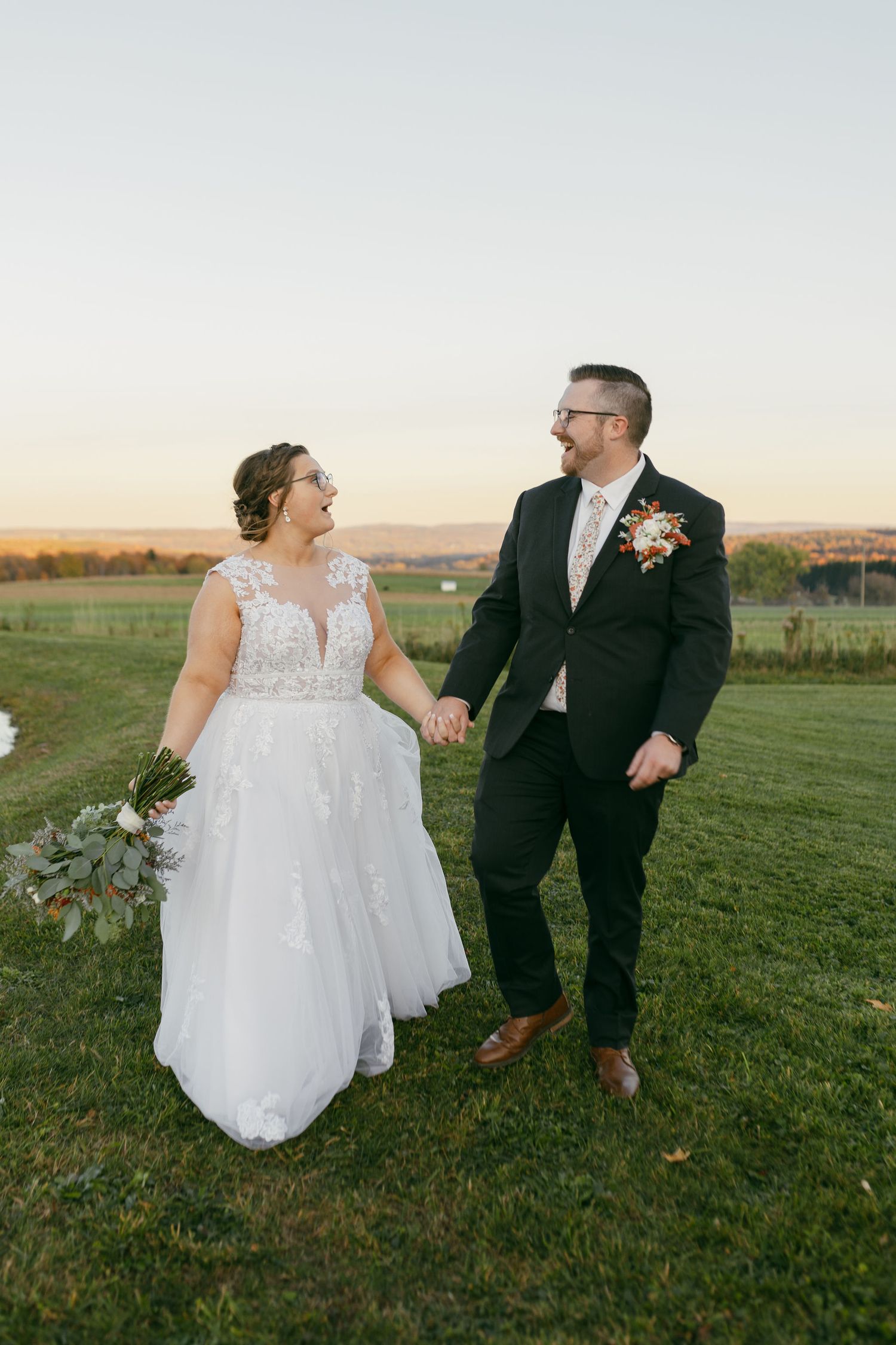 Wedding couple walking together on a grassy hilltop during golden hour sunset.