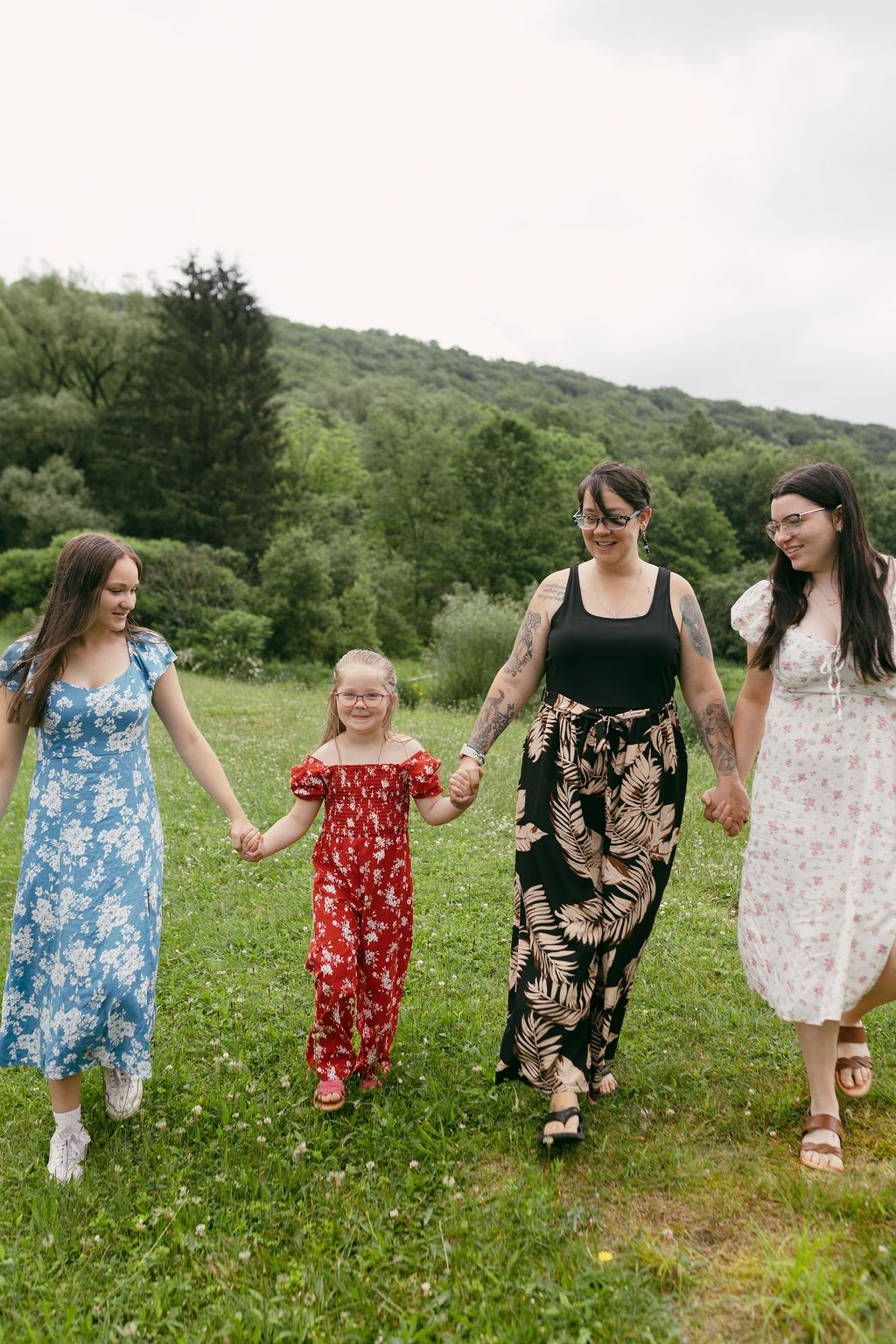 A group walks hand in hand through a wildflower meadow wearing coordinated summer dresses.