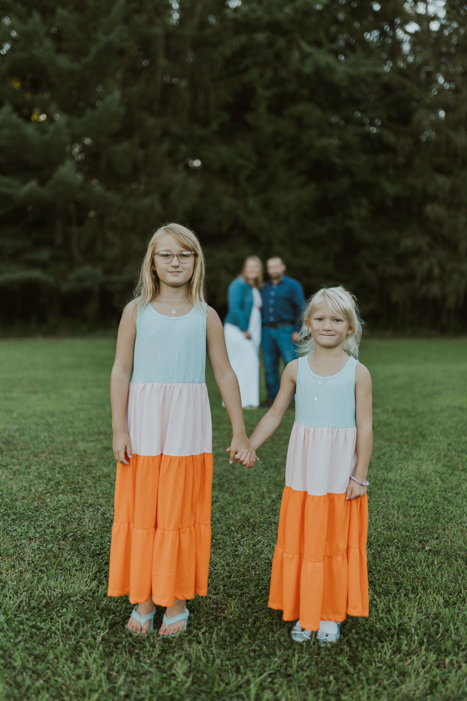 Two people in matching orange and white dresses standing in a green field.