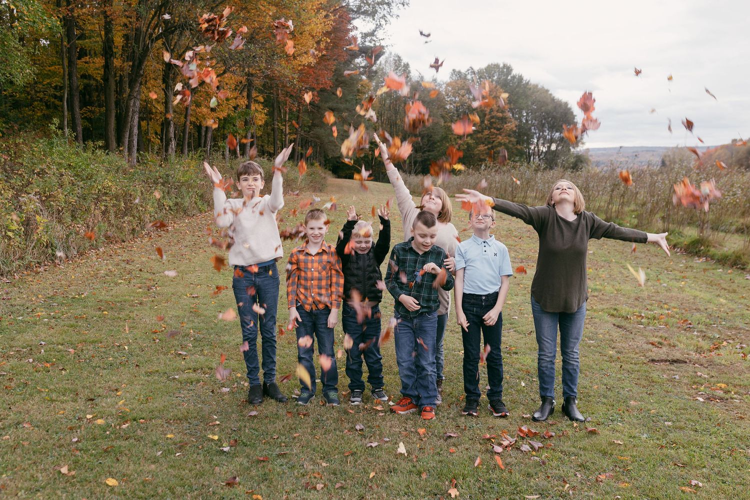 A group playfully throws autumn leaves in the air while standing on a grassy hillside.
