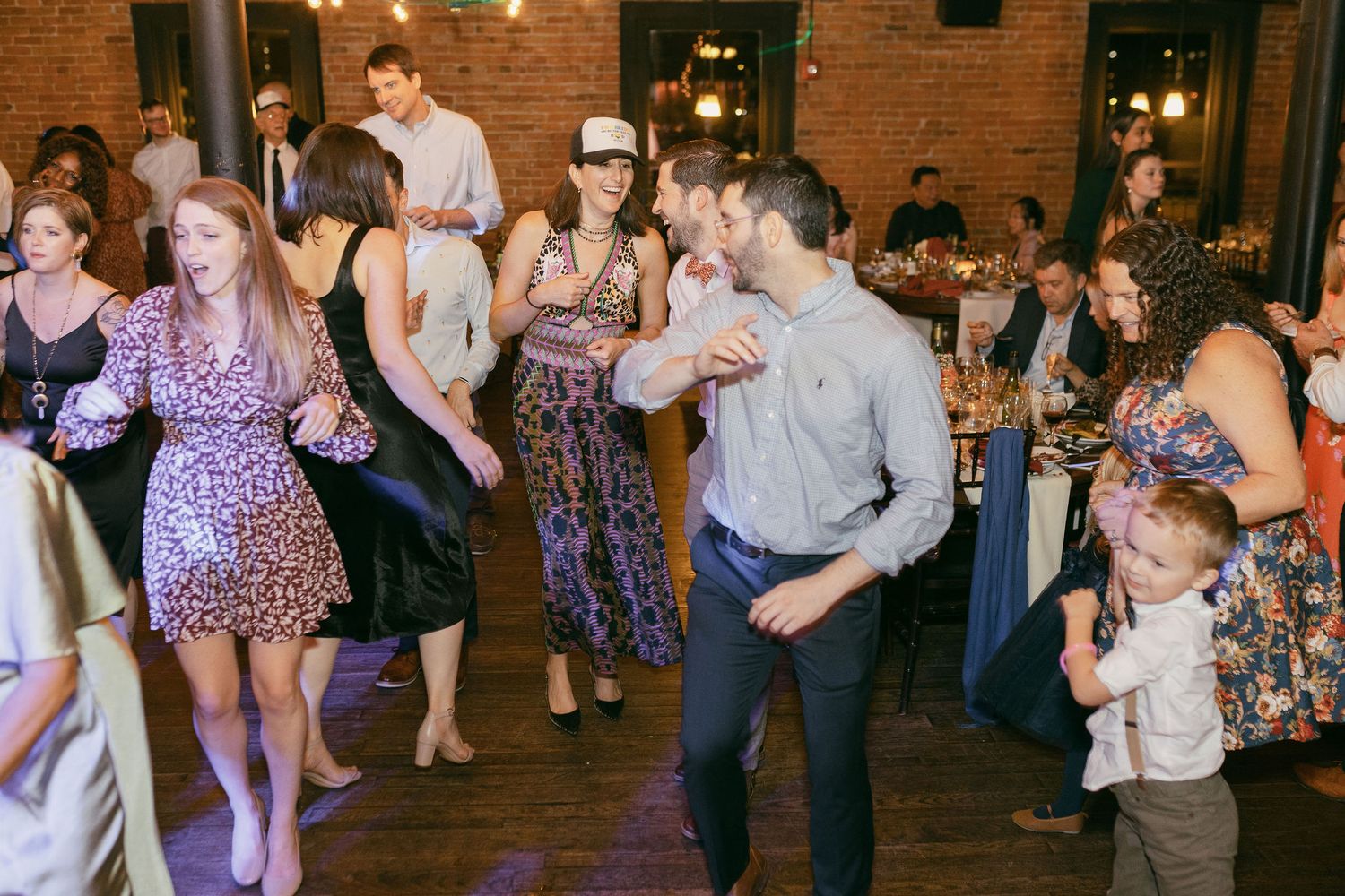 Wedding reception dance floor filled with guests under string lights in brick venue.