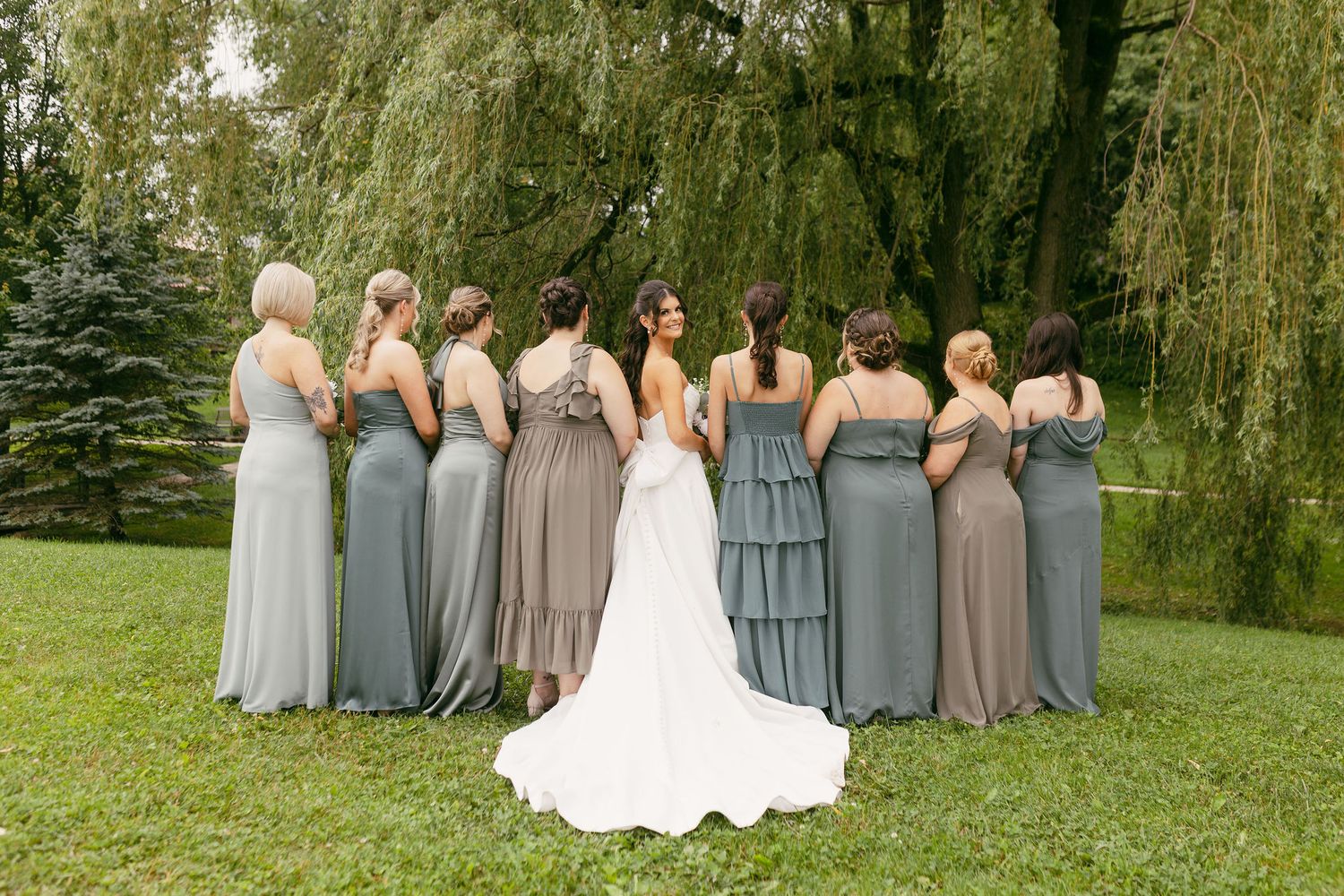 Wedding party poses under weeping willow trees in coordinated grey and navy attire.
