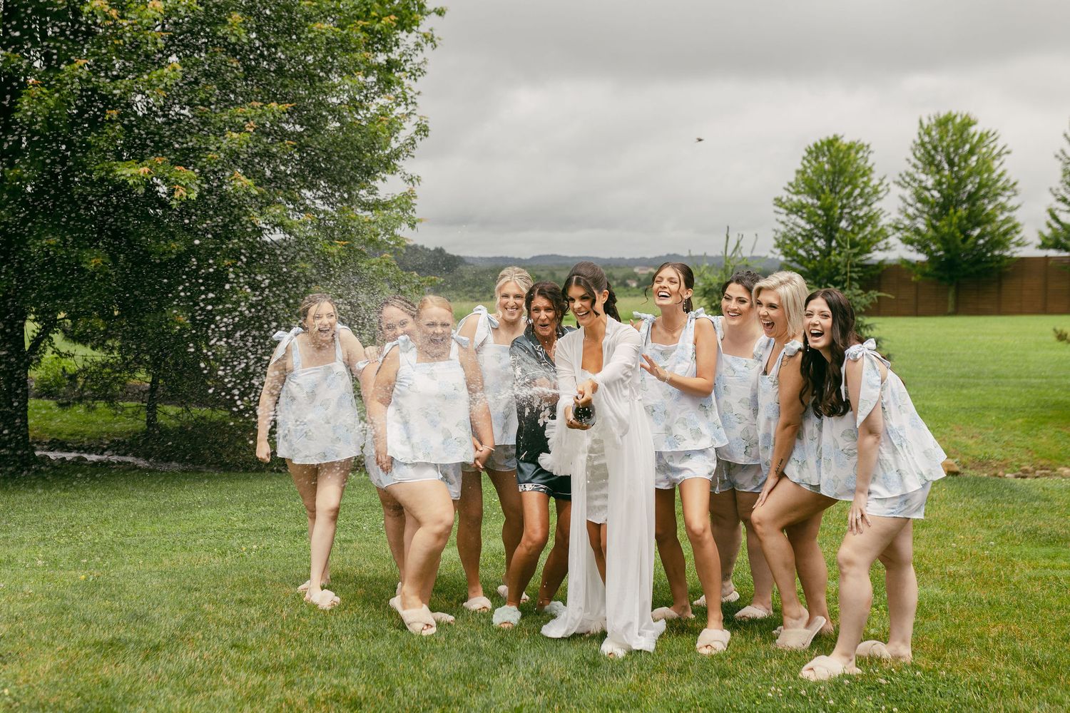 Wedding party members in white dresses and casual footwear pose together outdoors.