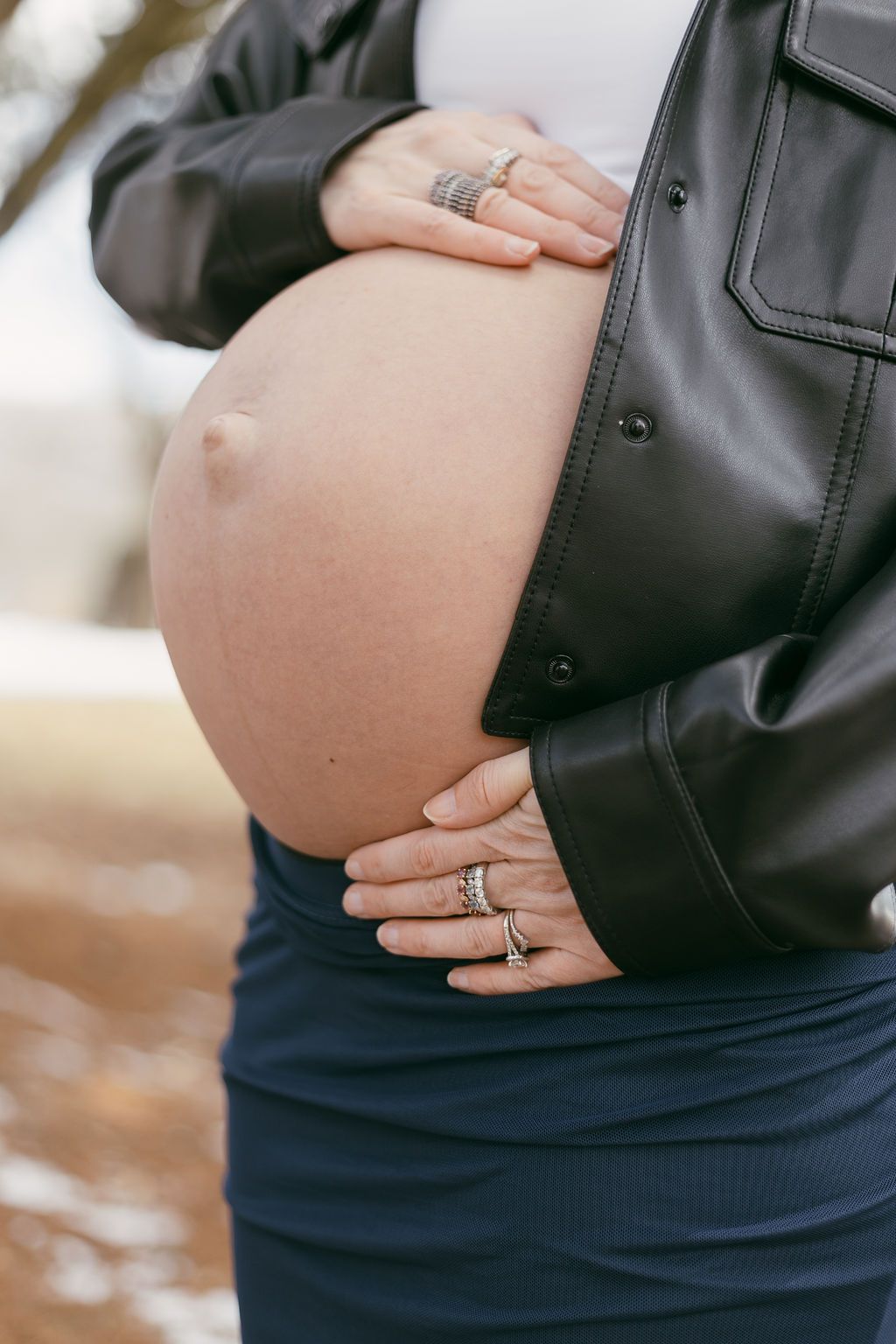 Close-up of hands cradling pregnant belly showing wedding rings.