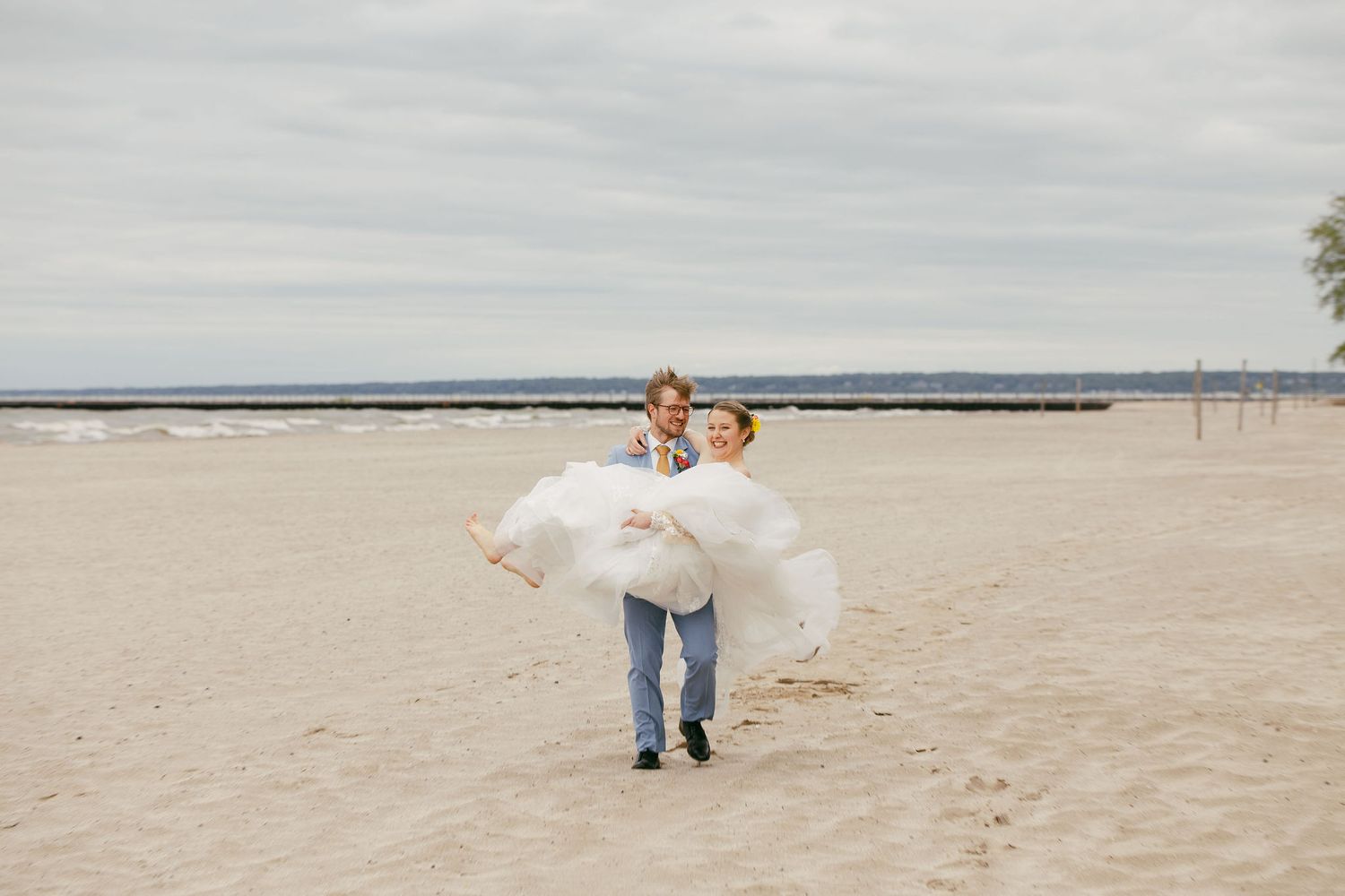 Couple walks along a sandy beach with a scenic water view in the background.