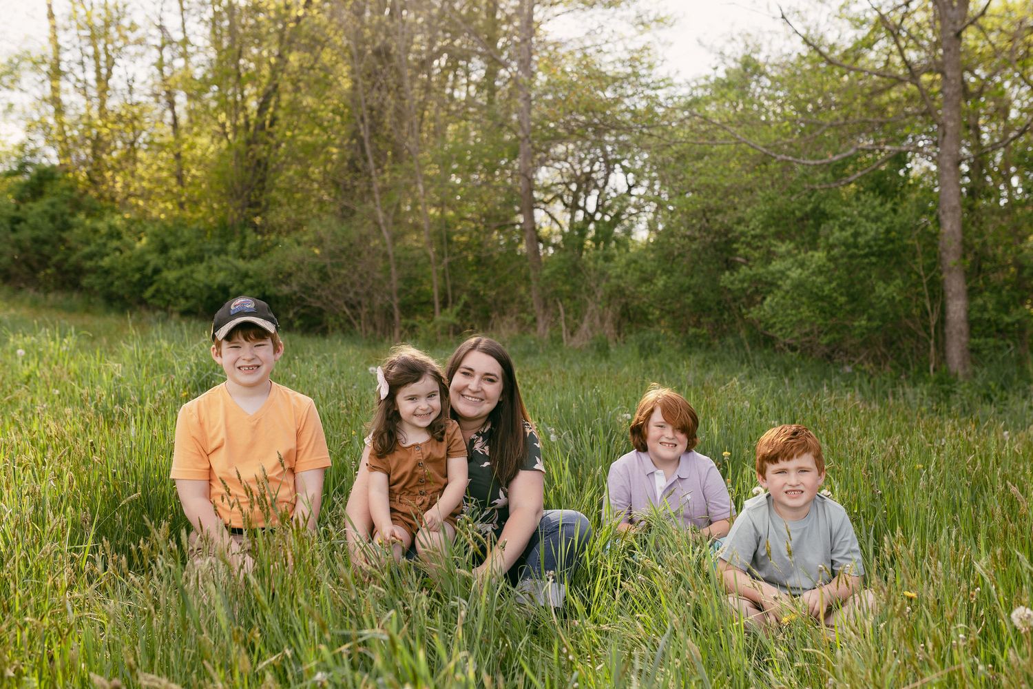 Family group sitting together in tall grass during an outdoor photo session.