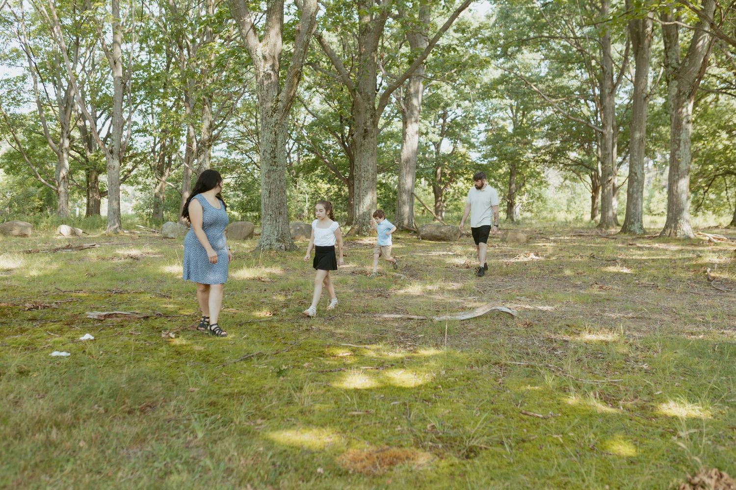 Family of four playing outdoors in a lush green woodland park on a sunny day.