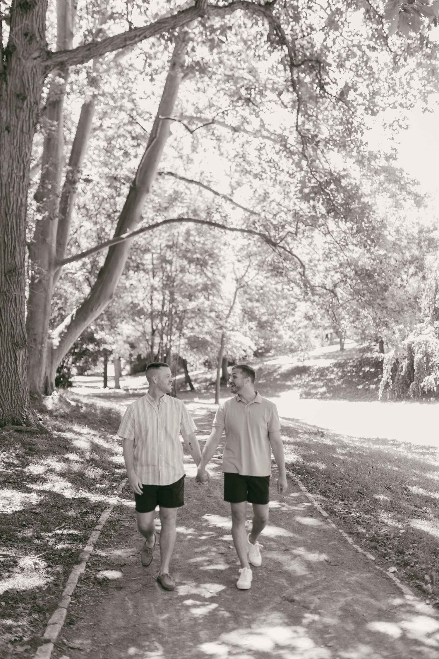 A couple walks hand in hand down a tree-lined path on a sunny summer day.