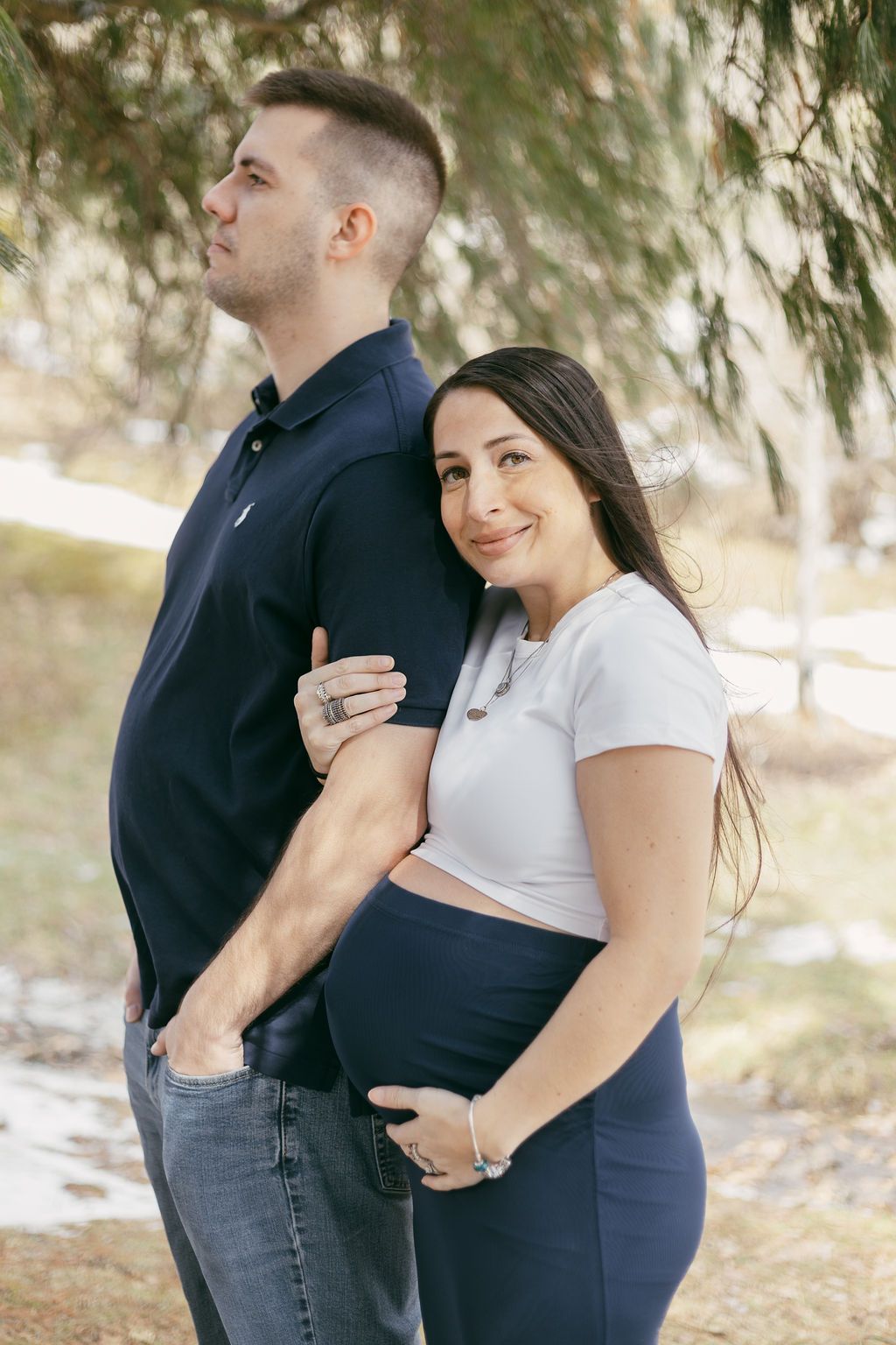 Loving couple embracing outdoors in casual attire under evergreen trees.