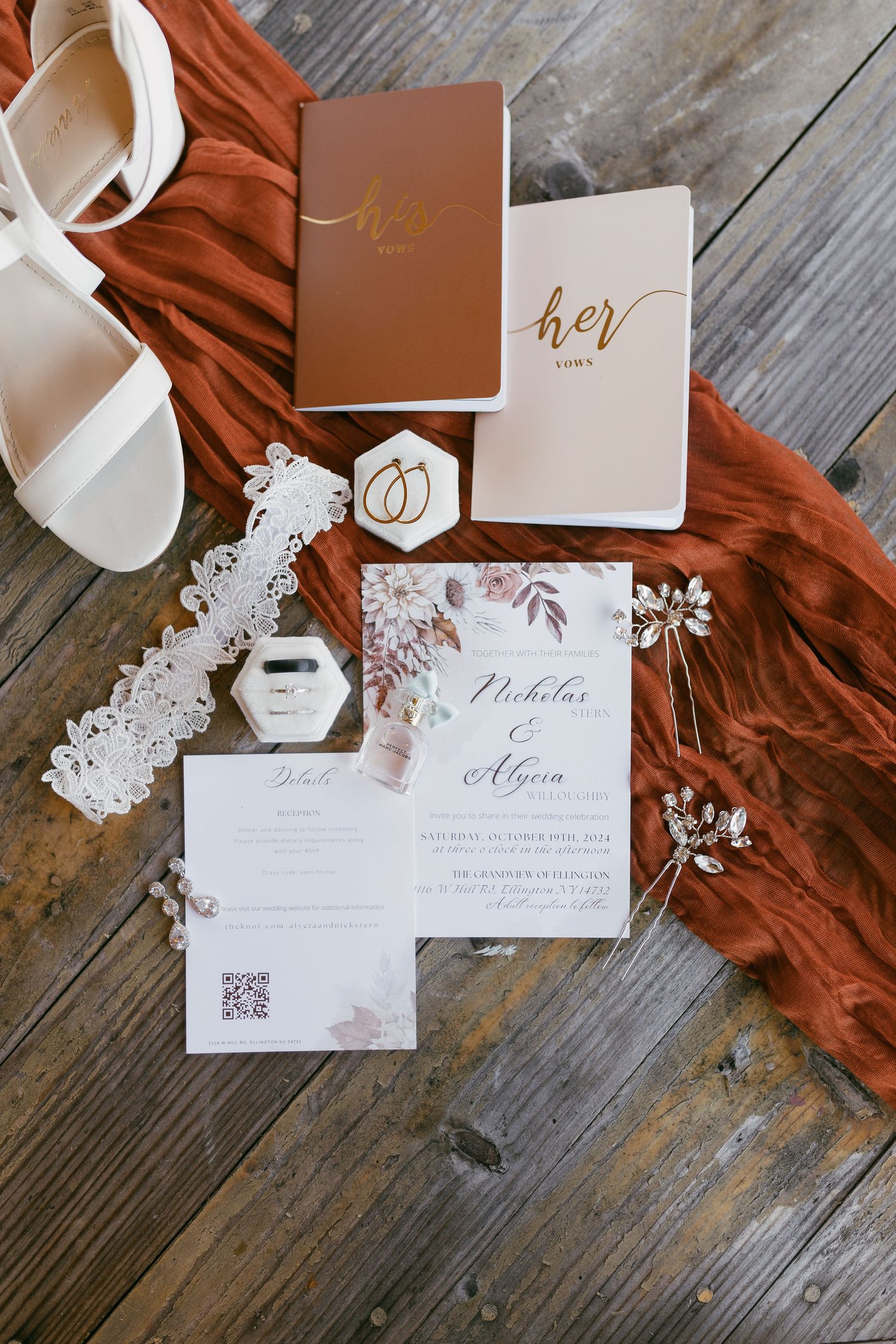 Wedding invitation suite with white and terracotta details laid out on wooden surface.