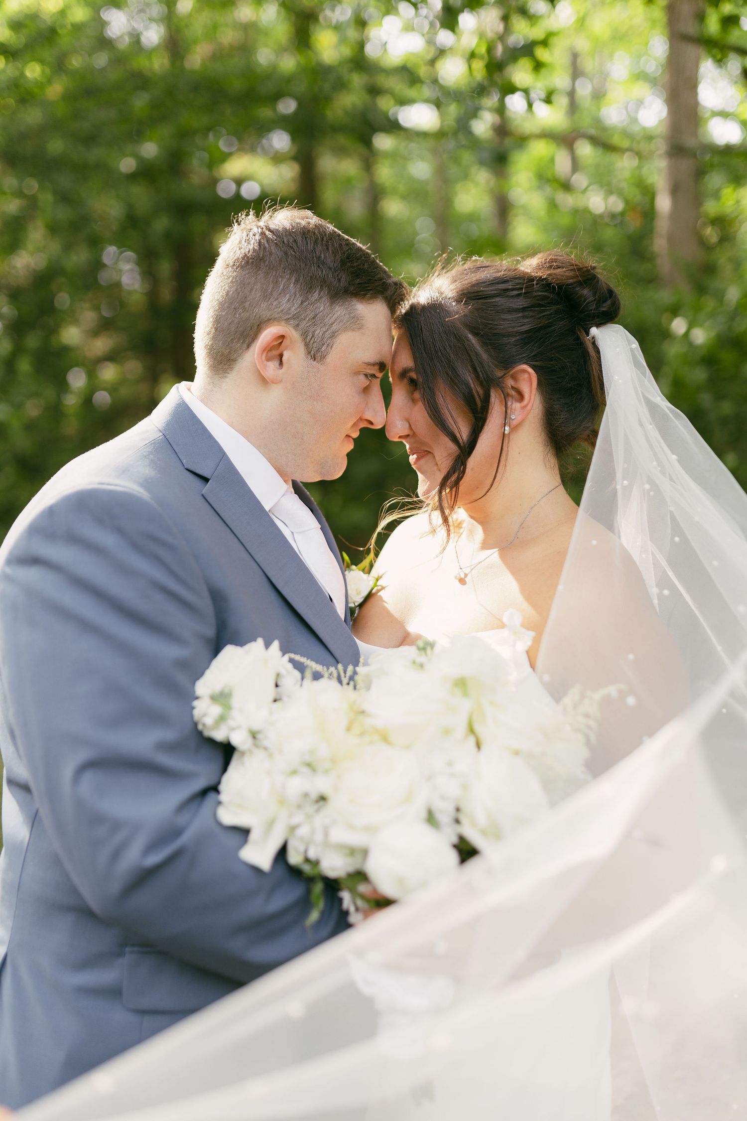 Intimate moment between newlyweds with white bouquet and flowing veil.