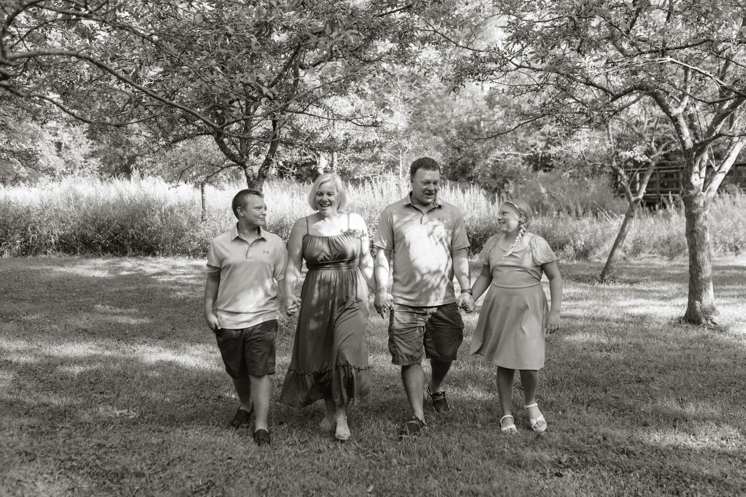 Black and white photo of a family of five walking together through a lush green park with trees.