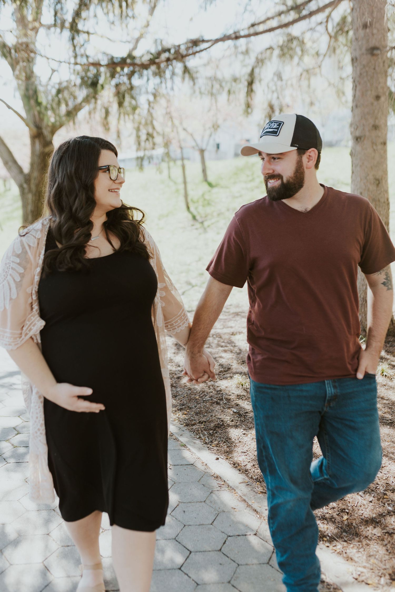 Casual couple walking and laughing together along a tree-lined path.
