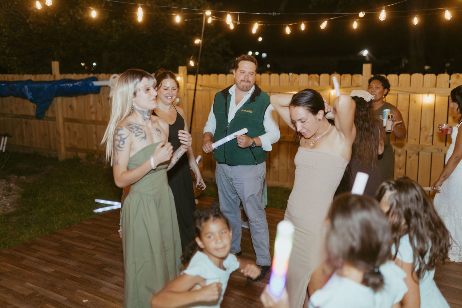 Guests dancing and celebrating outdoors at night wedding reception with string lights.