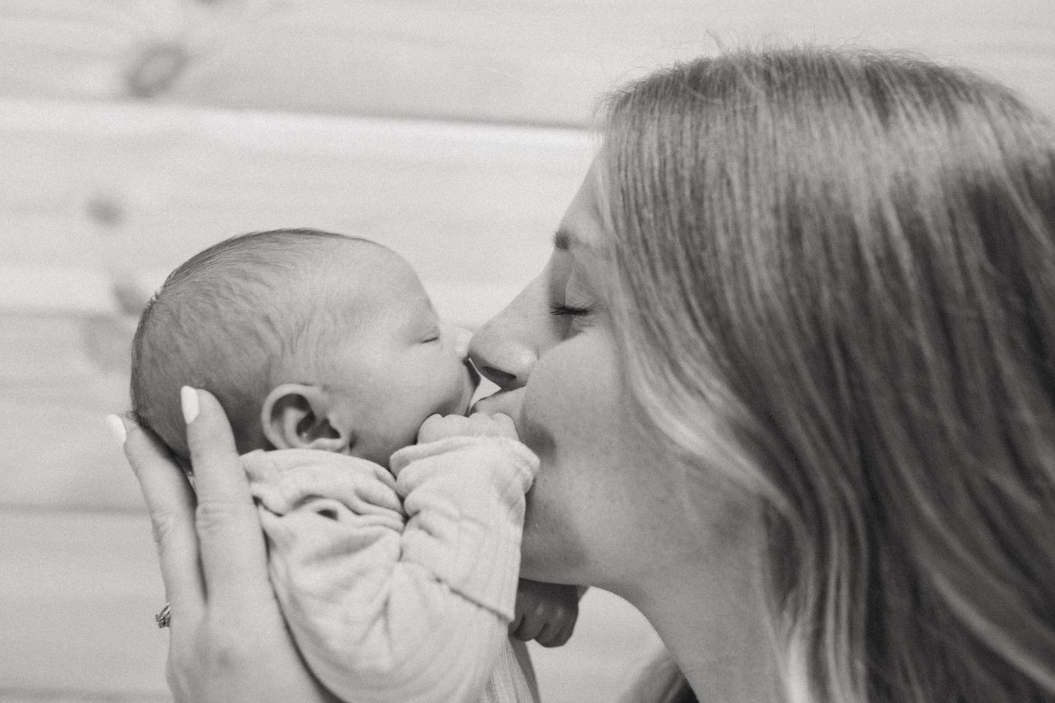 Black and white photo of a loving mother gently kissing her newborn baby, holding the infant close to her face.